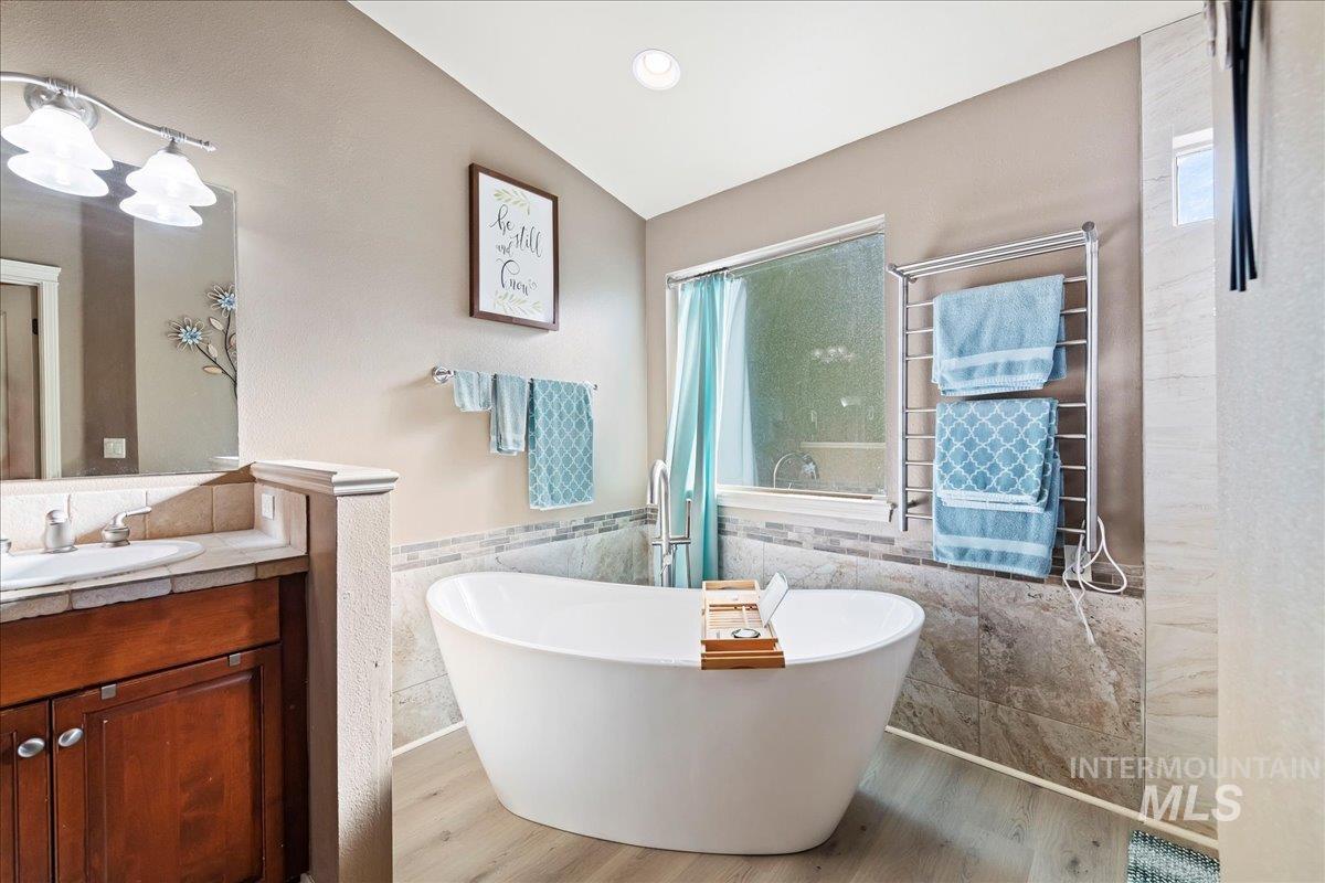 Full bath with tile walls, light wood-style floors, vanity, a freestanding tub, and wainscoting