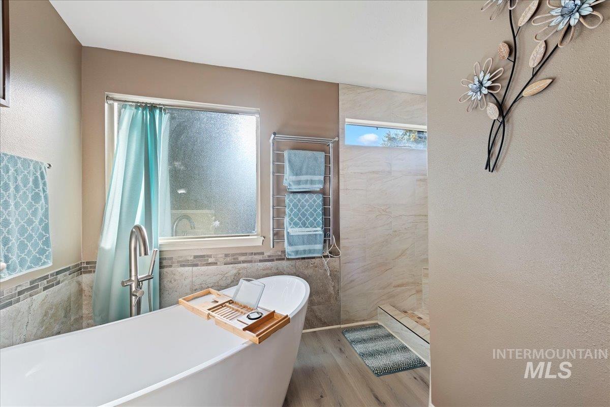 Full bath with tile walls, wood finished floors, a freestanding tub, and a walk in shower