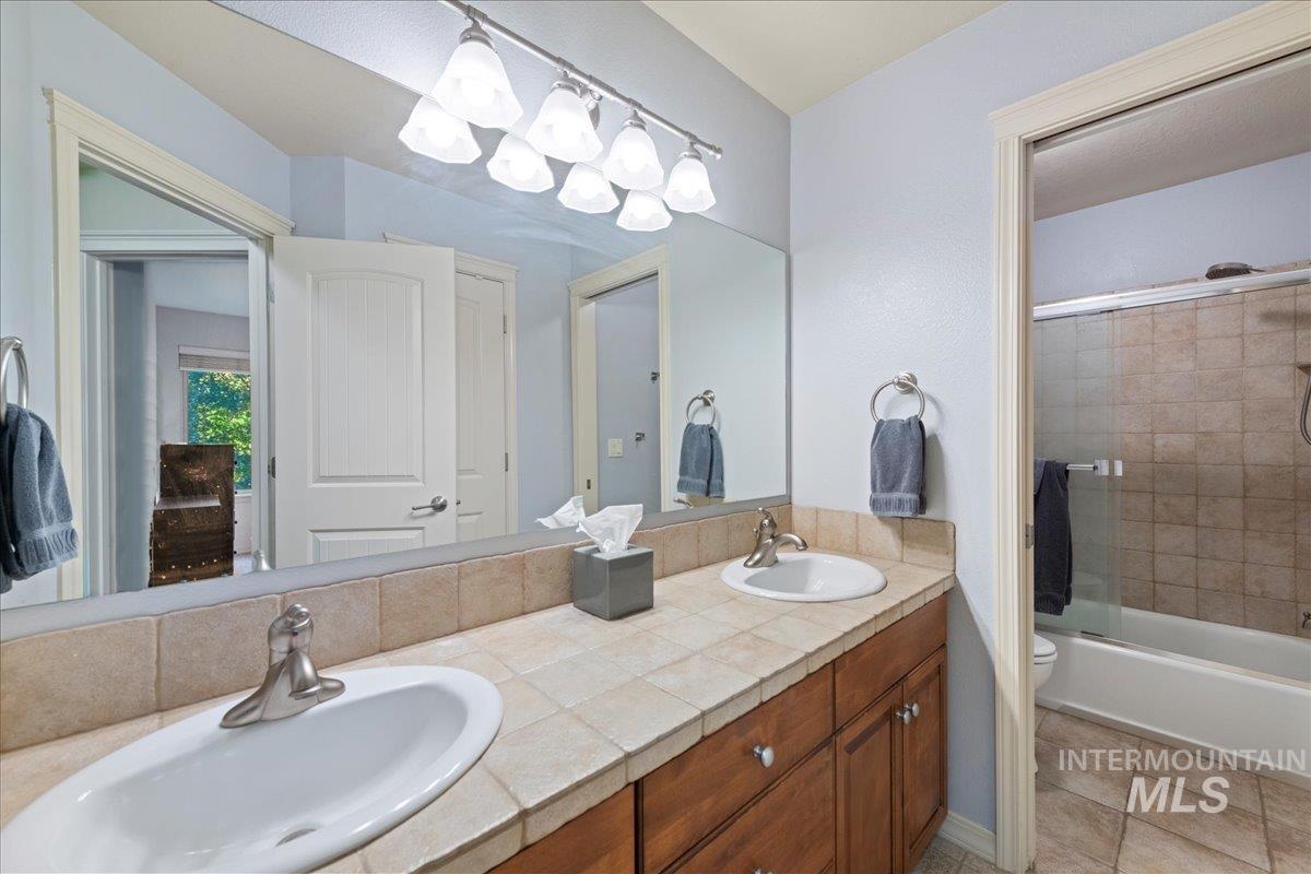 Full bath with shower / bath combination with glass door, double vanity, and light tile patterned floors