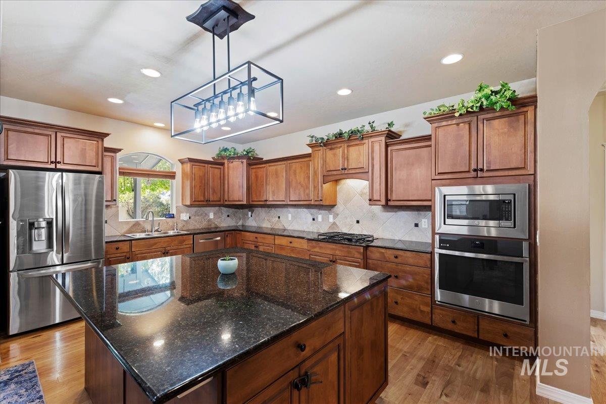 Kitchen with appliances with stainless steel finishes, backsplash, a kitchen island, dark stone countertops, and light wood-style floors