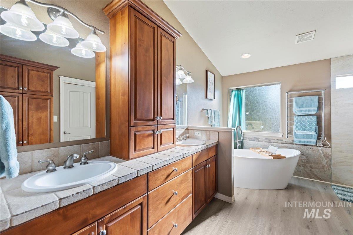 Full bathroom with a freestanding tub, light wood-style flooring, double vanity, tile walls, and lofted ceiling