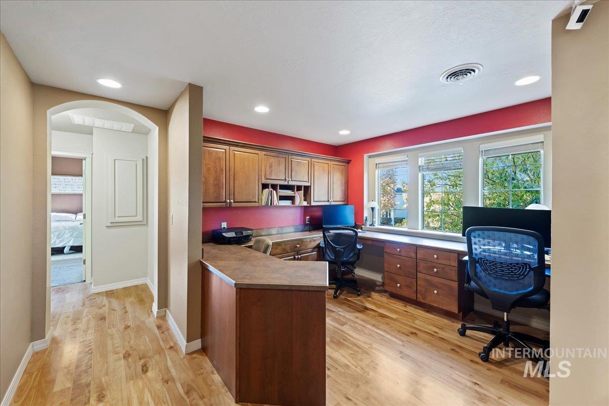 Office space featuring built in study area, light wood finished floors, arched walkways, and recessed lighting