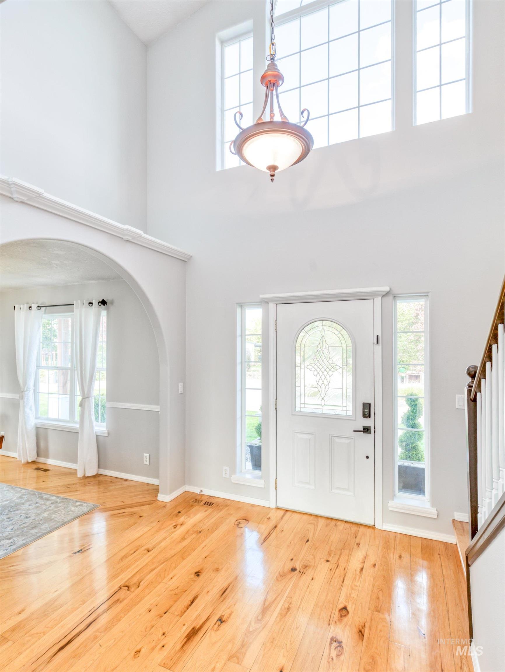 Foyer featuring arched walkways, a towering ceiling, light wood-style flooring, and stairs