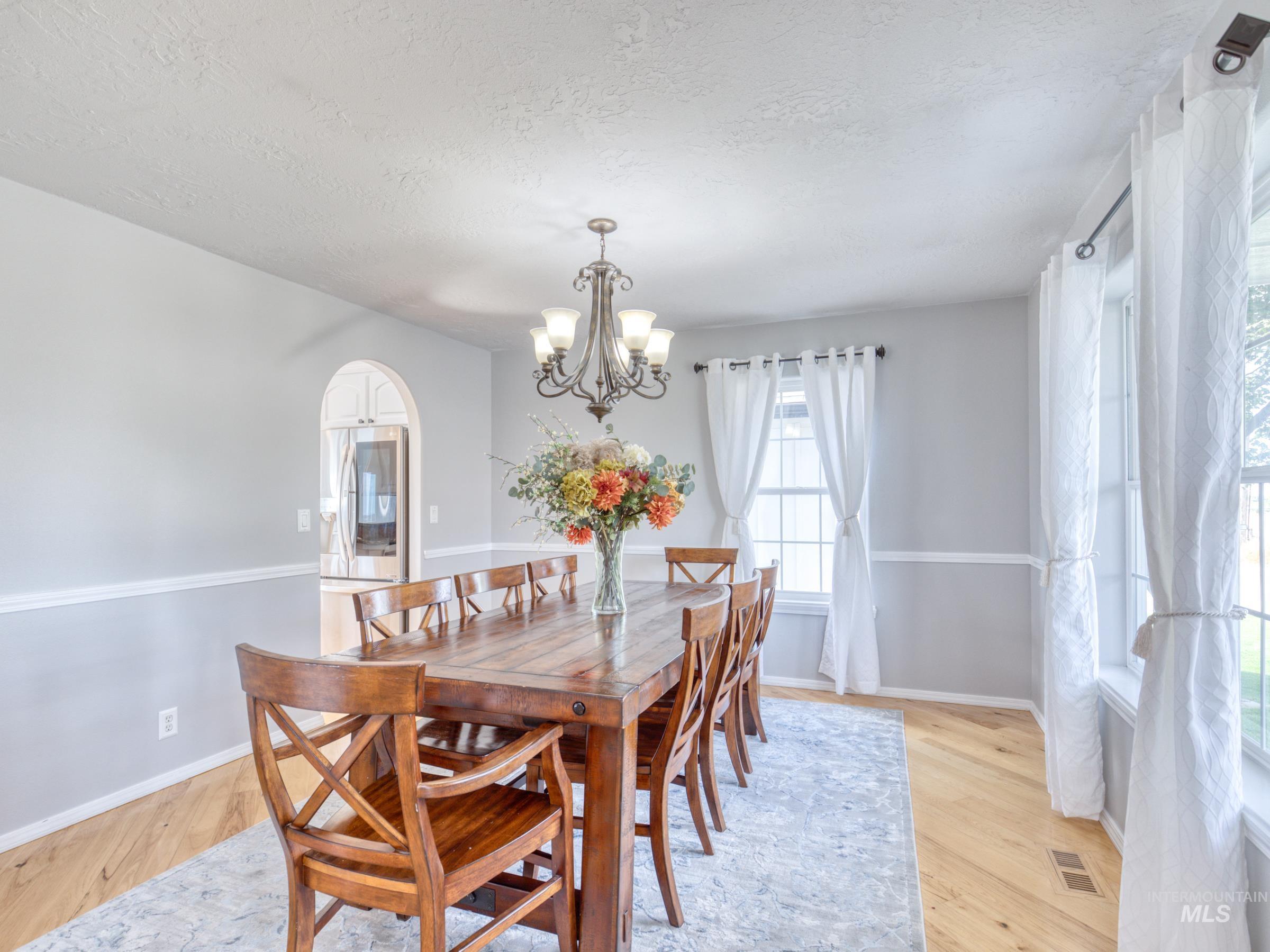 Dining room featuring light wood-type flooring, arched walkways, a chandelier, and a textured ceiling