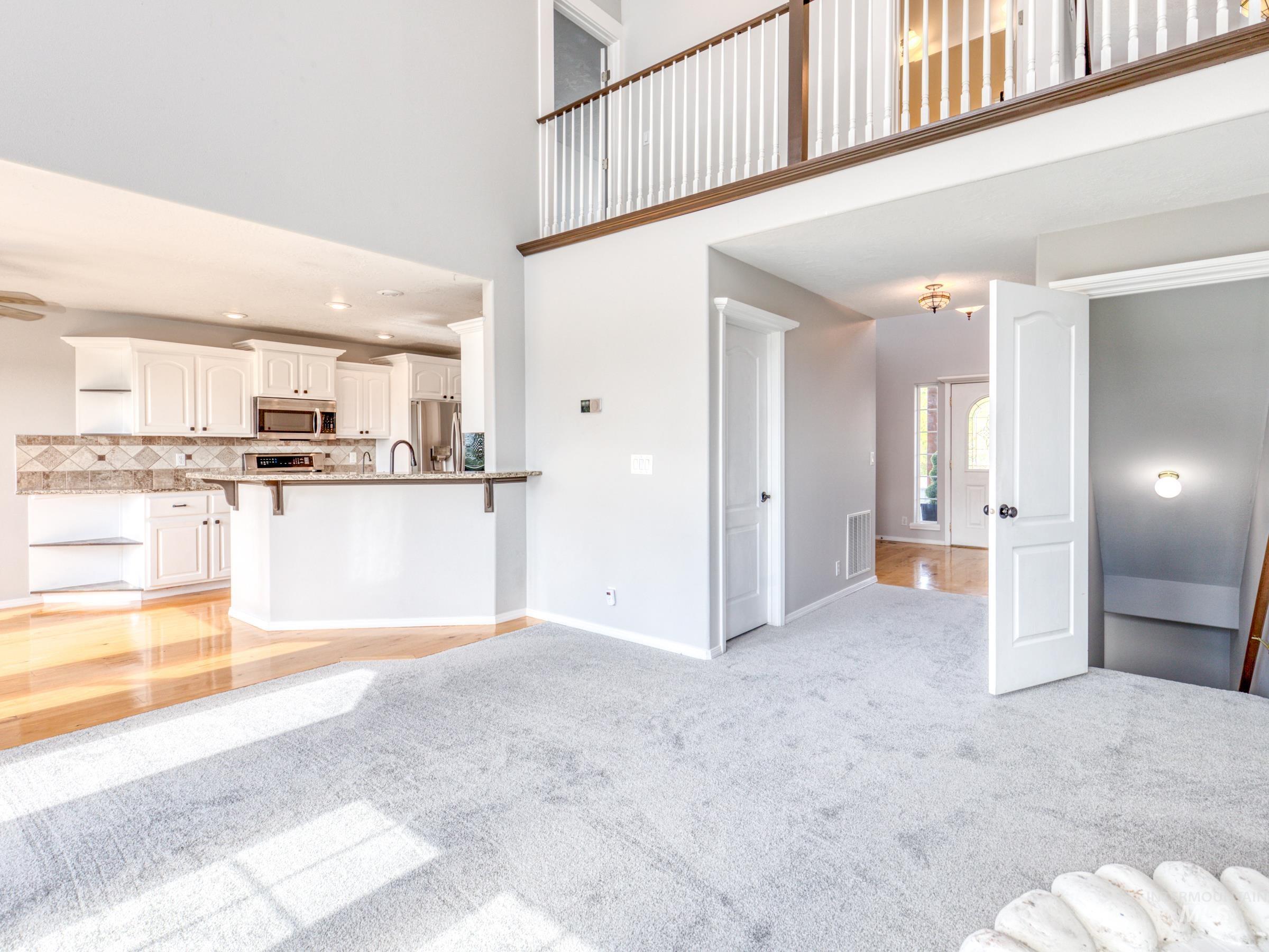 Unfurnished living room with a towering ceiling, light colored carpet, light wood-style floors, and recessed lighting