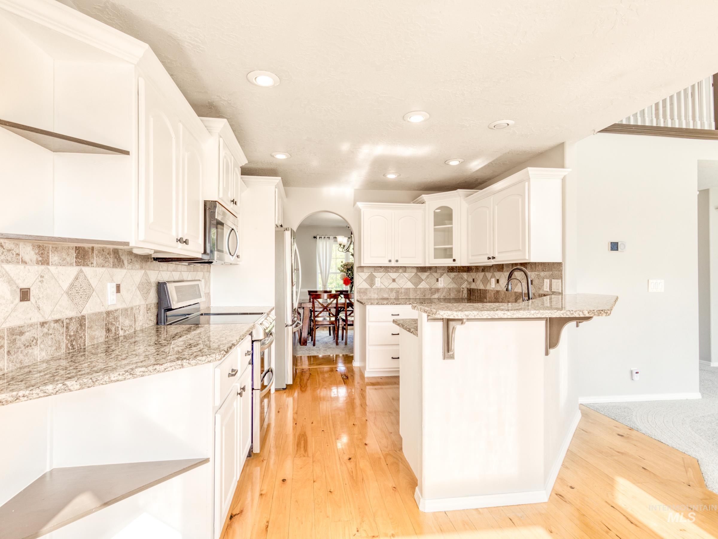 Kitchen featuring arched walkways, stainless steel appliances, a kitchen breakfast bar, white cabinetry, and a peninsula