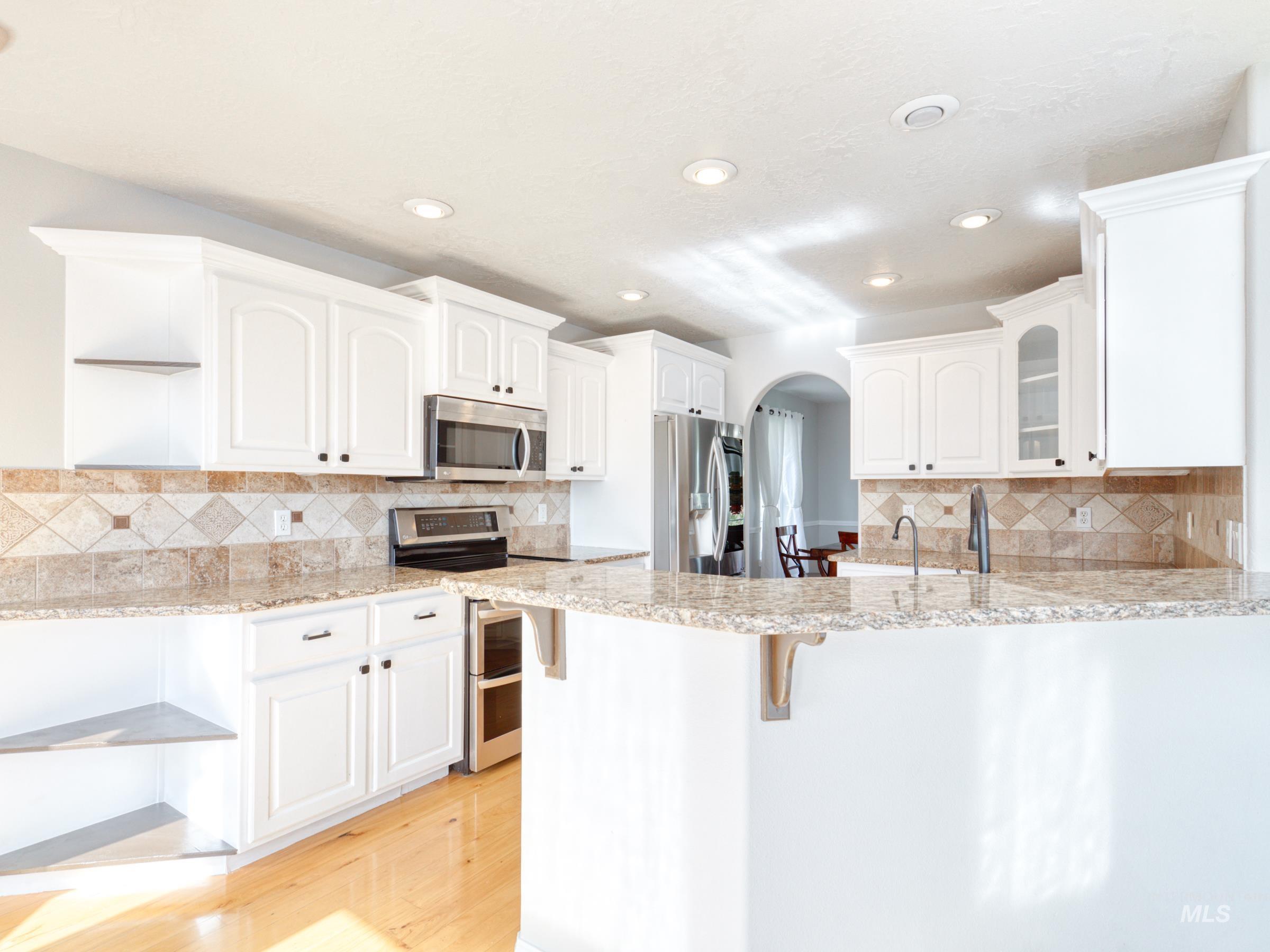 Kitchen featuring arched walkways, appliances with stainless steel finishes, a breakfast bar area, white cabinets, and glass insert cabinets