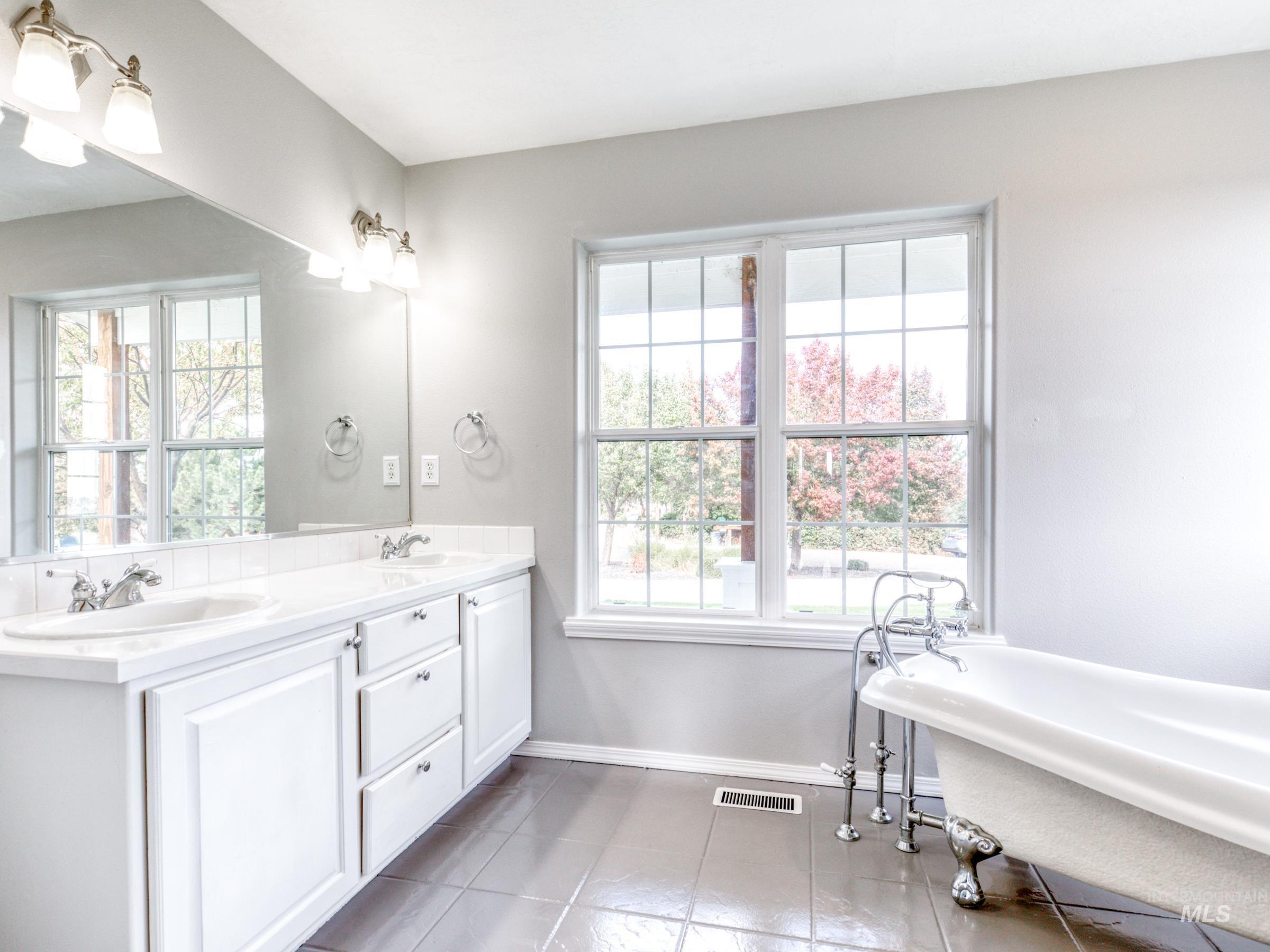 Full bathroom featuring a soaking tub, double vanity, plenty of natural light, and light tile patterned floors