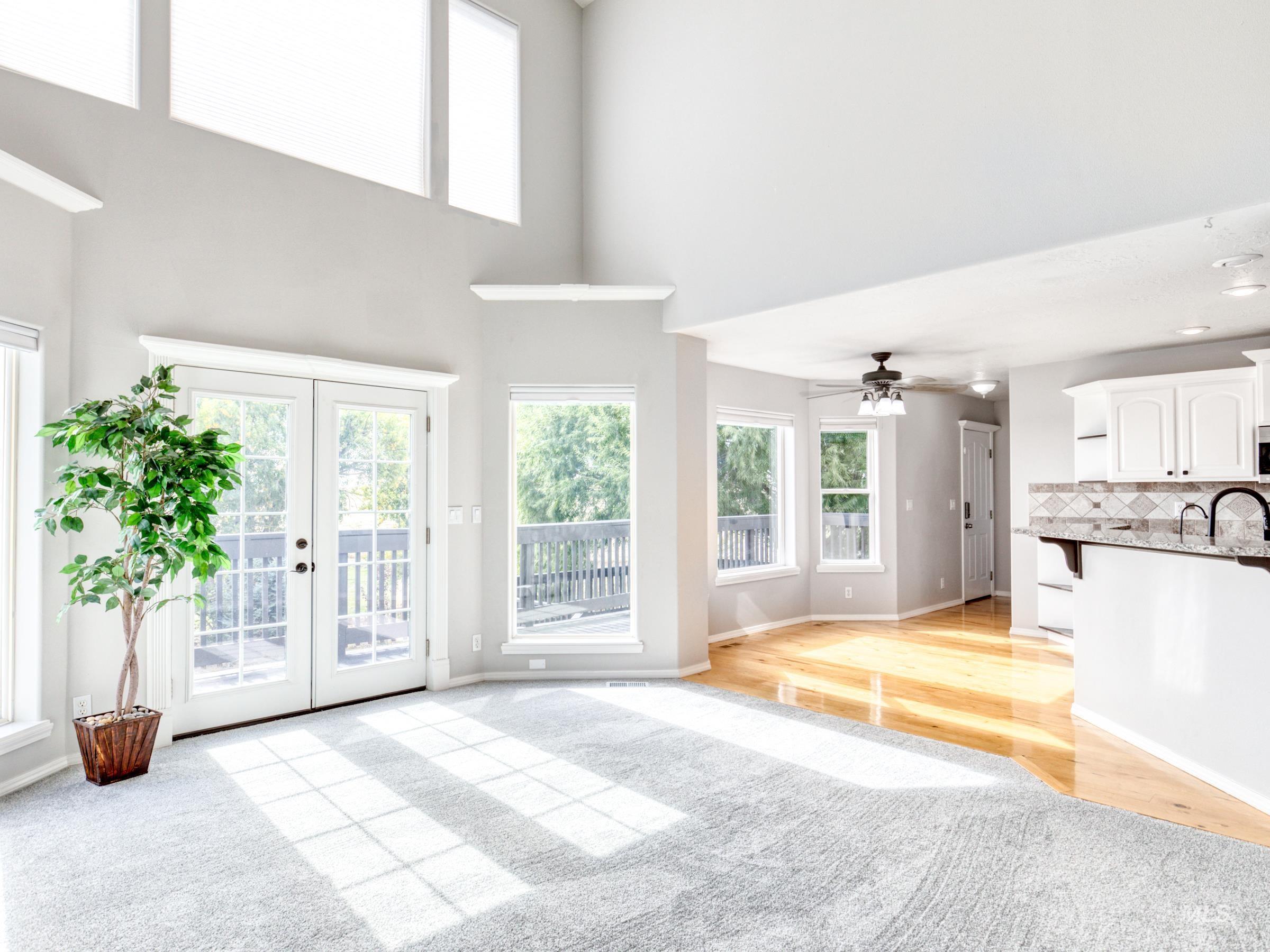 Unfurnished living room featuring a high ceiling, french doors, a ceiling fan, light wood-type flooring, and light carpet