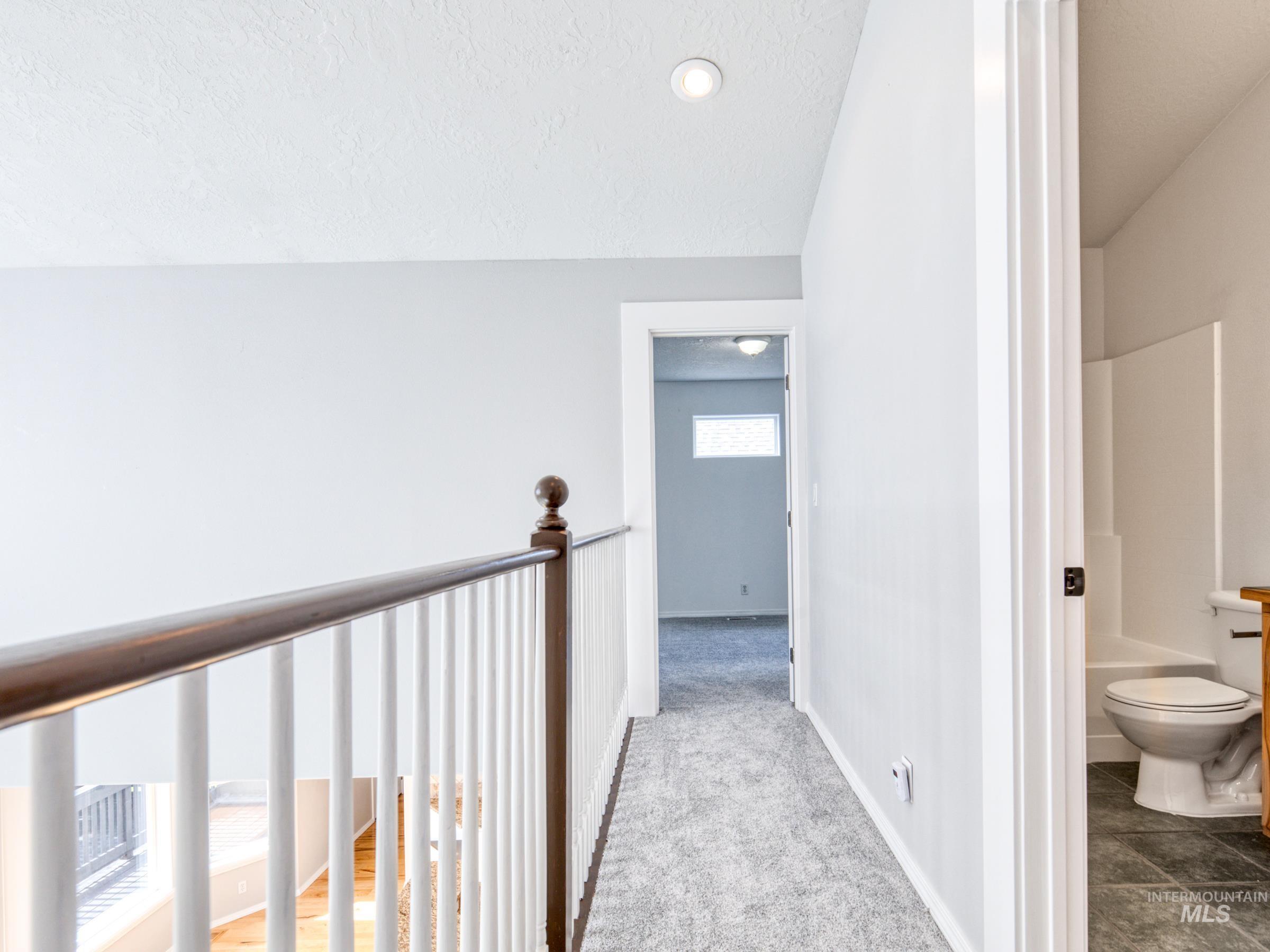 Hallway featuring carpet, a textured ceiling, lofted ceiling, and an upstairs landing