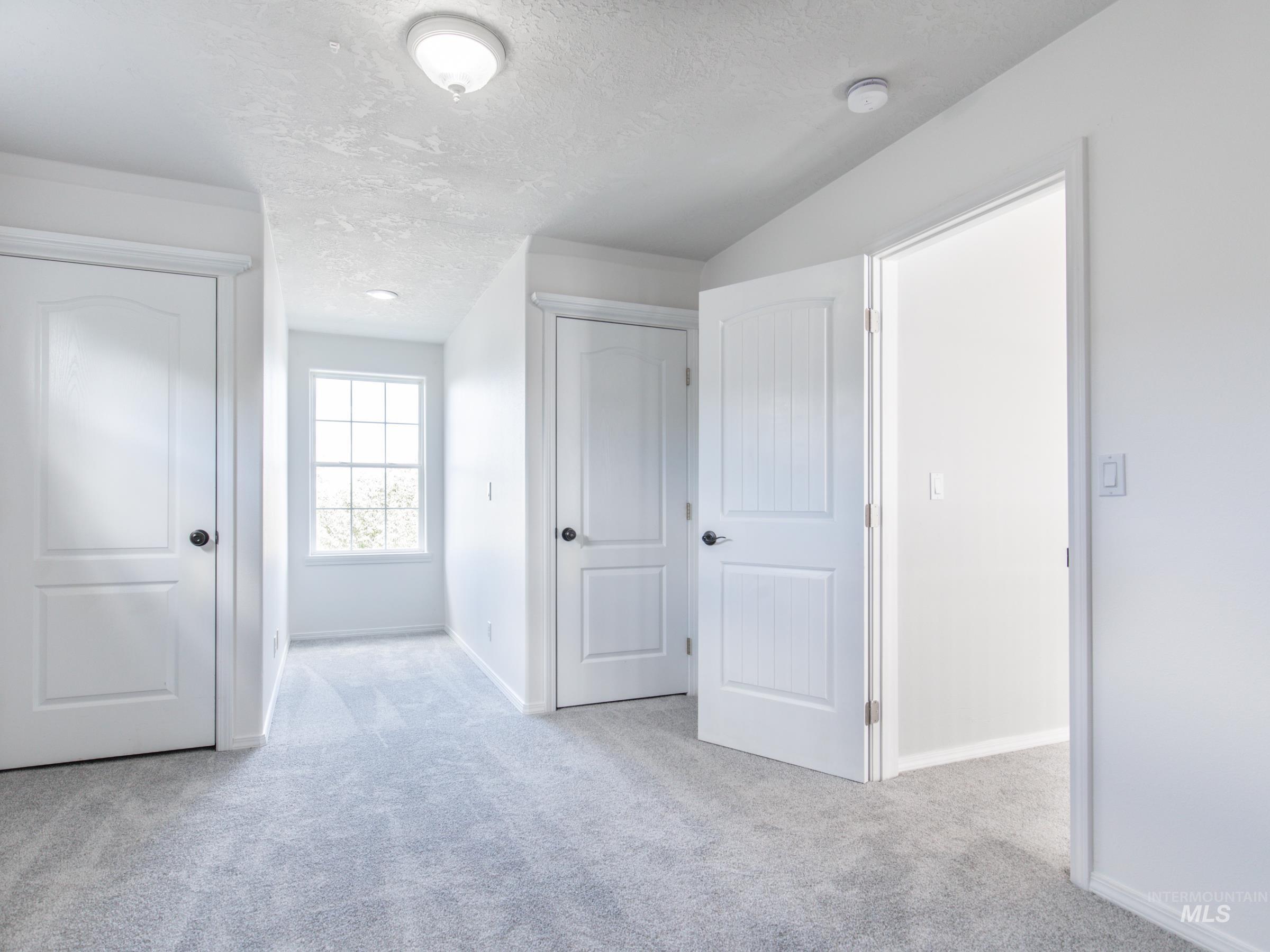 Unfurnished bedroom with a textured ceiling, light carpet, and two closets