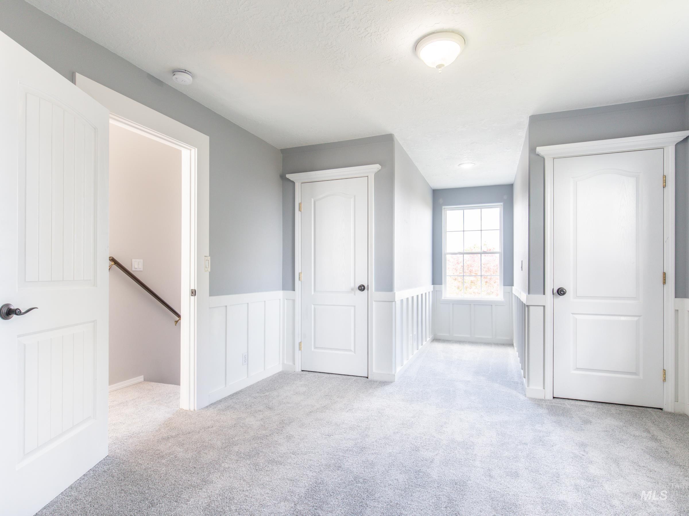 Unfurnished bedroom featuring light colored carpet, a wainscoted wall, and a decorative wall