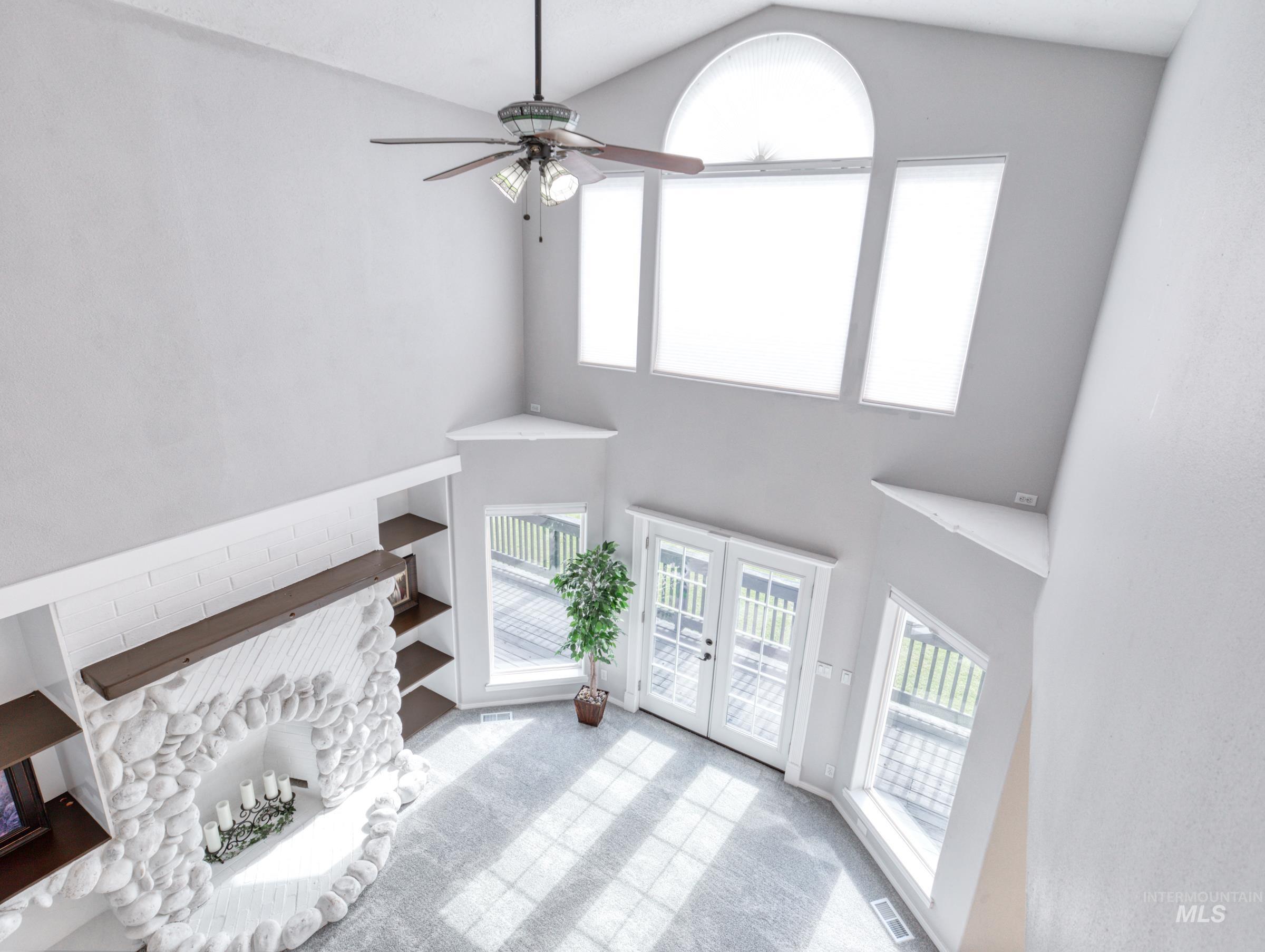 Unfurnished living room featuring plenty of natural light, carpet flooring, french doors, high vaulted ceiling, and a ceiling fan