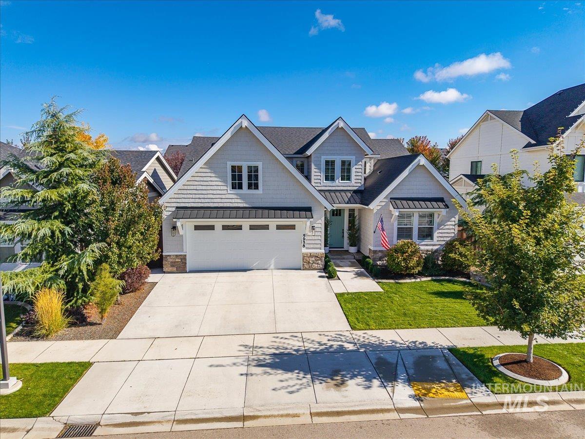Craftsman-style home featuring a standing seam roof, a metal roof, stone siding, concrete driveway, and a garage
