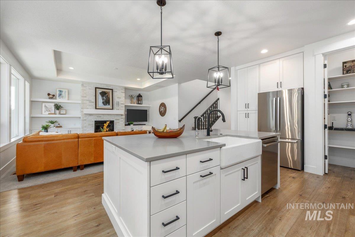 Kitchen with open floor plan, white cabinetry, stainless steel appliances, a tray ceiling, and hanging light fixtures