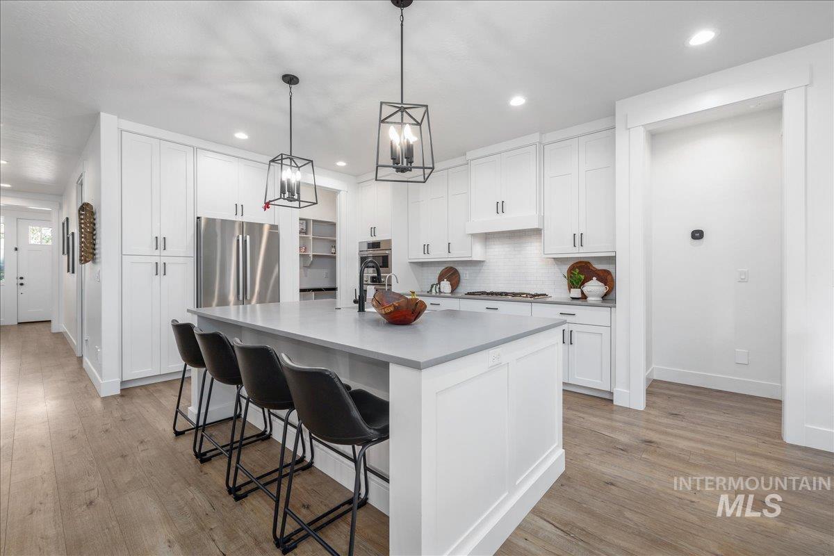 Kitchen featuring a kitchen bar, backsplash, an island with sink, appliances with stainless steel finishes, and light wood finished floors