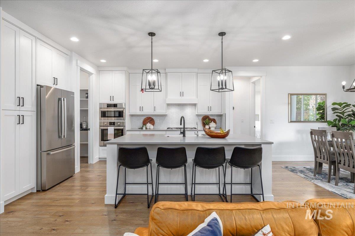 Kitchen featuring appliances with stainless steel finishes, hanging light fixtures, a breakfast bar, a center island with sink, and tasteful backsplash