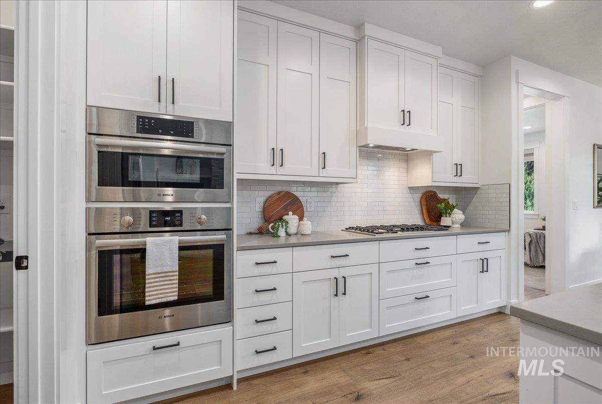 Kitchen featuring appliances with stainless steel finishes, white cabinetry, light wood finished floors, decorative backsplash, and recessed lighting