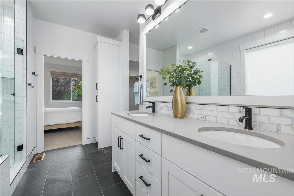 Full bathroom featuring a shower stall, double vanity, connected bathroom, and decorative backsplash