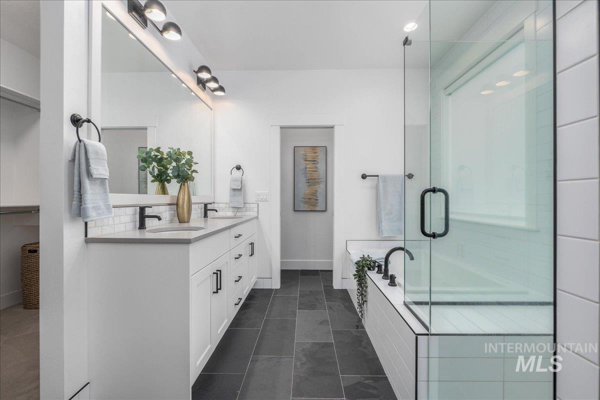 Full bathroom with double vanity, a garden tub, a stall shower, dark tile patterned floors, and a closet