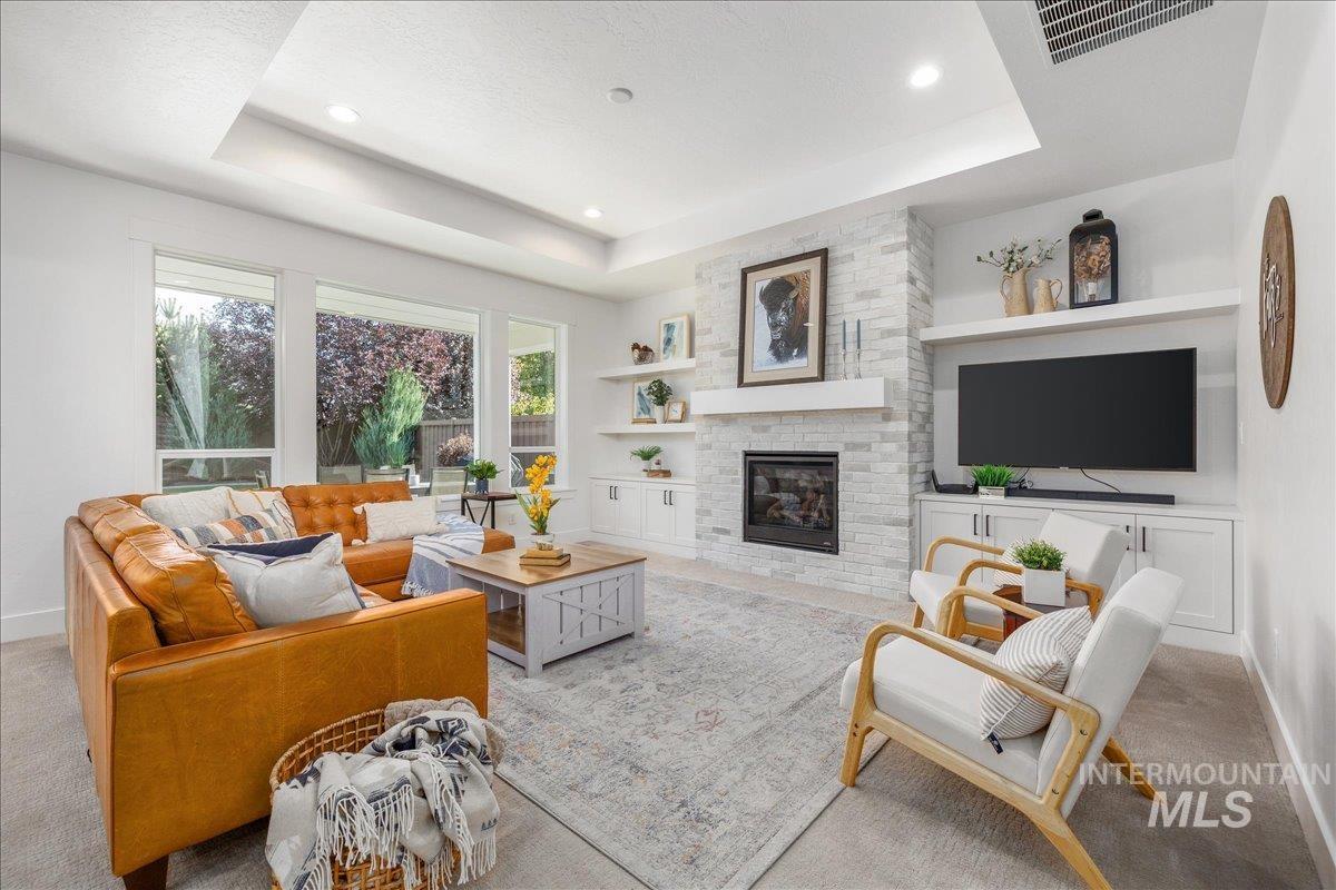 Living room with carpet flooring, a tray ceiling, built in features, a large fireplace, and recessed lighting