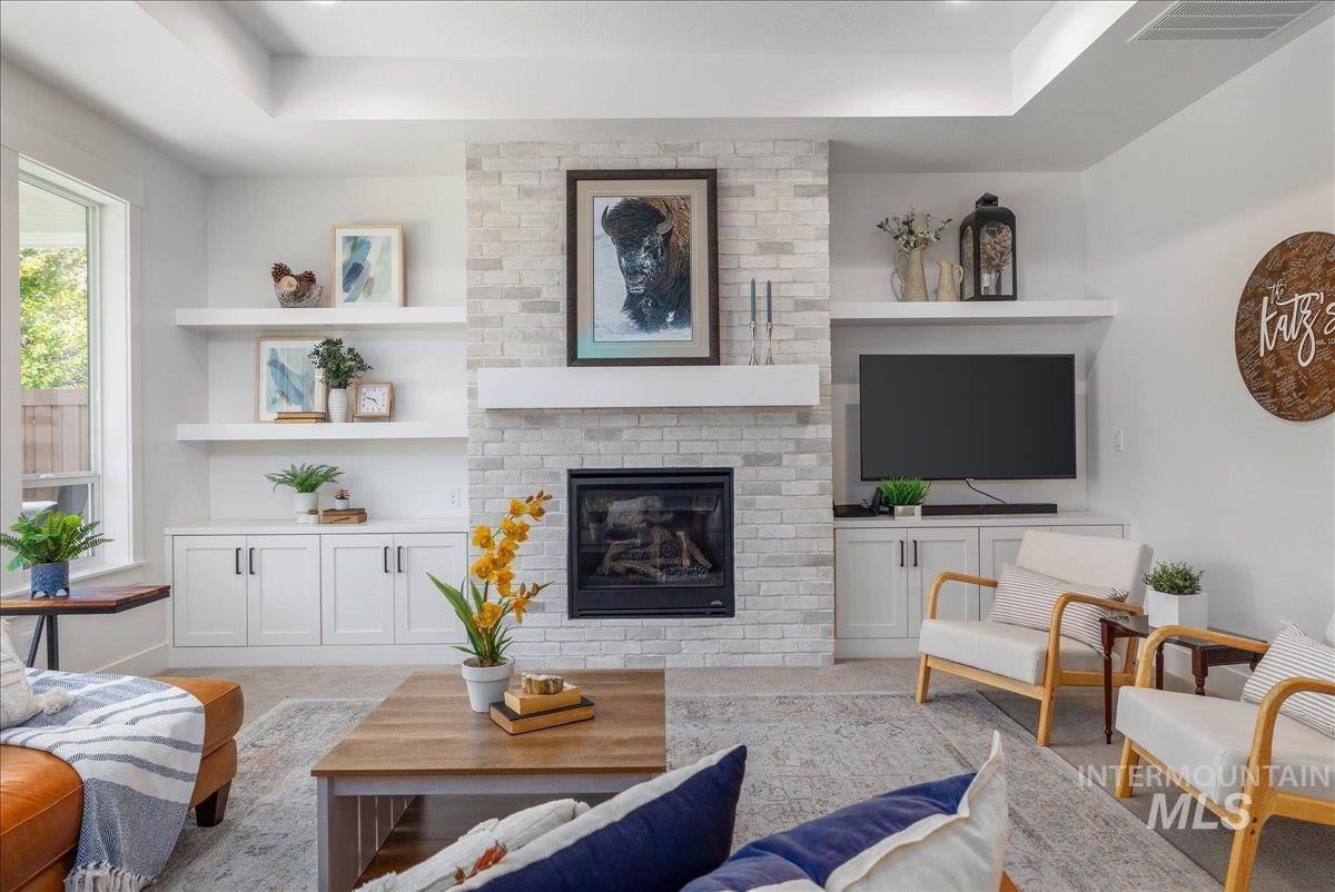 Living room with a tray ceiling, a brick fireplace, light colored carpet, and built in features