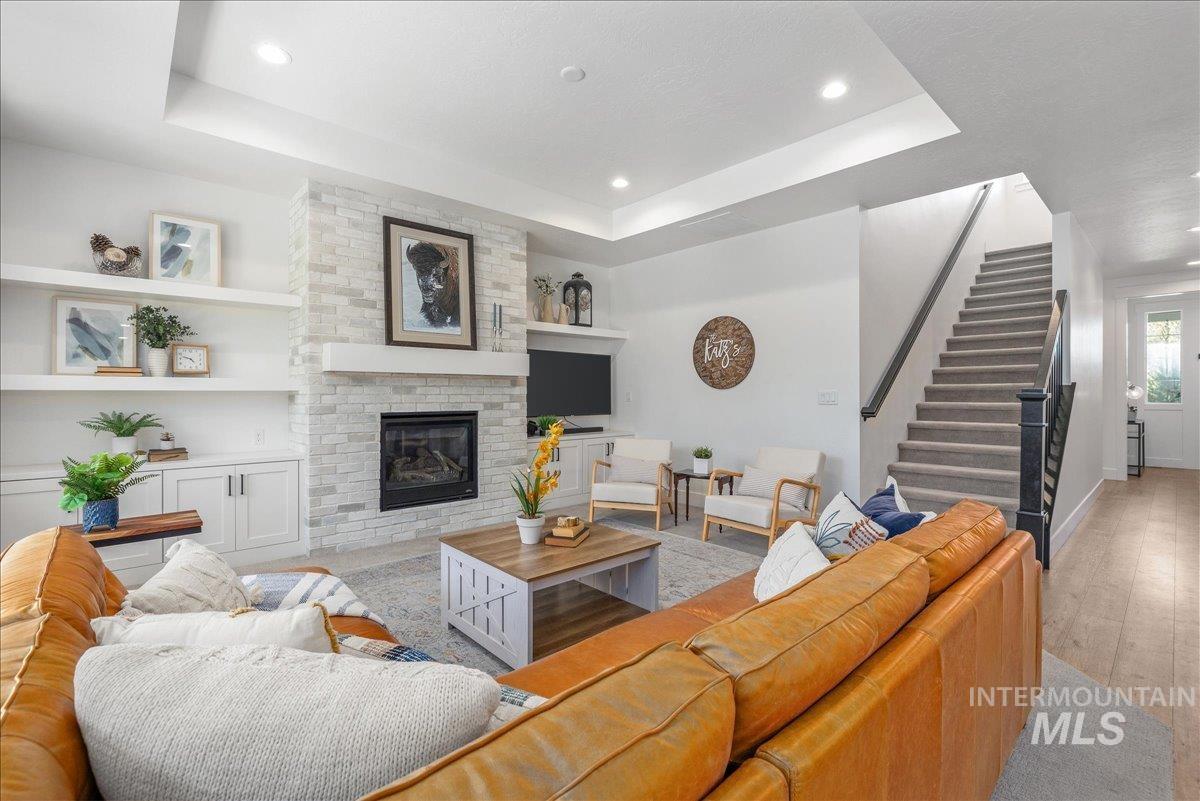 Living room featuring a tray ceiling, stairs, a brick fireplace, recessed lighting, and light wood finished floors
