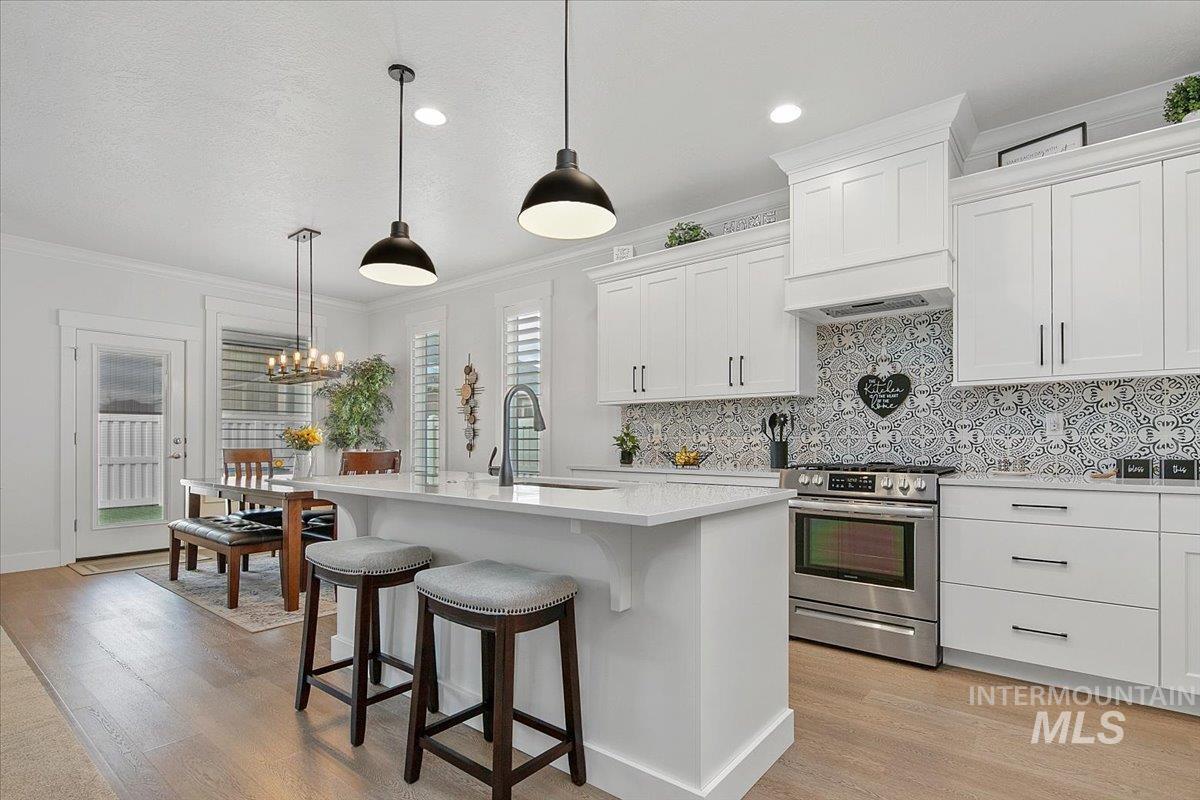 Kitchen featuring decorative backsplash, stainless steel electric stove, pendant lighting, white cabinets, and crown molding