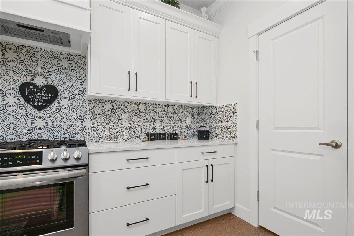 Kitchen featuring stainless steel range with gas cooktop, white cabinetry, exhaust hood, decorative backsplash, and light stone countertops