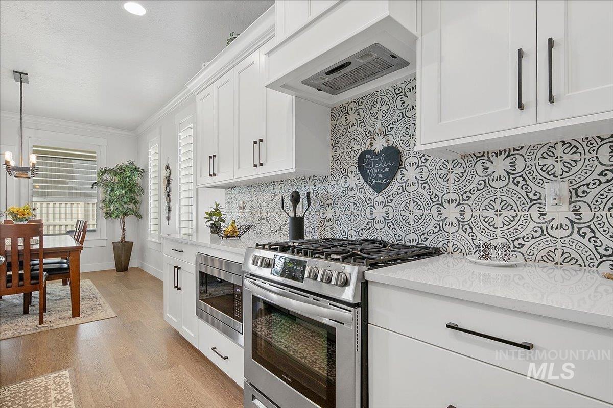 Kitchen with stainless steel appliances, premium range hood, white cabinetry, light wood-type flooring, and ornamental molding