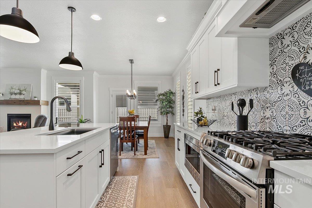 Kitchen with appliances with stainless steel finishes, white cabinetry, a glass covered fireplace, range hood, and a textured ceiling