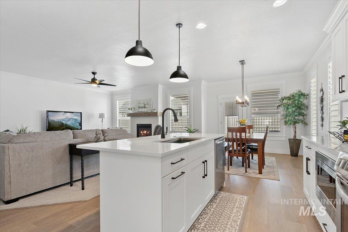 Kitchen featuring a warm lit fireplace, white cabinets, hanging light fixtures, ornamental molding, and light wood-style floors
