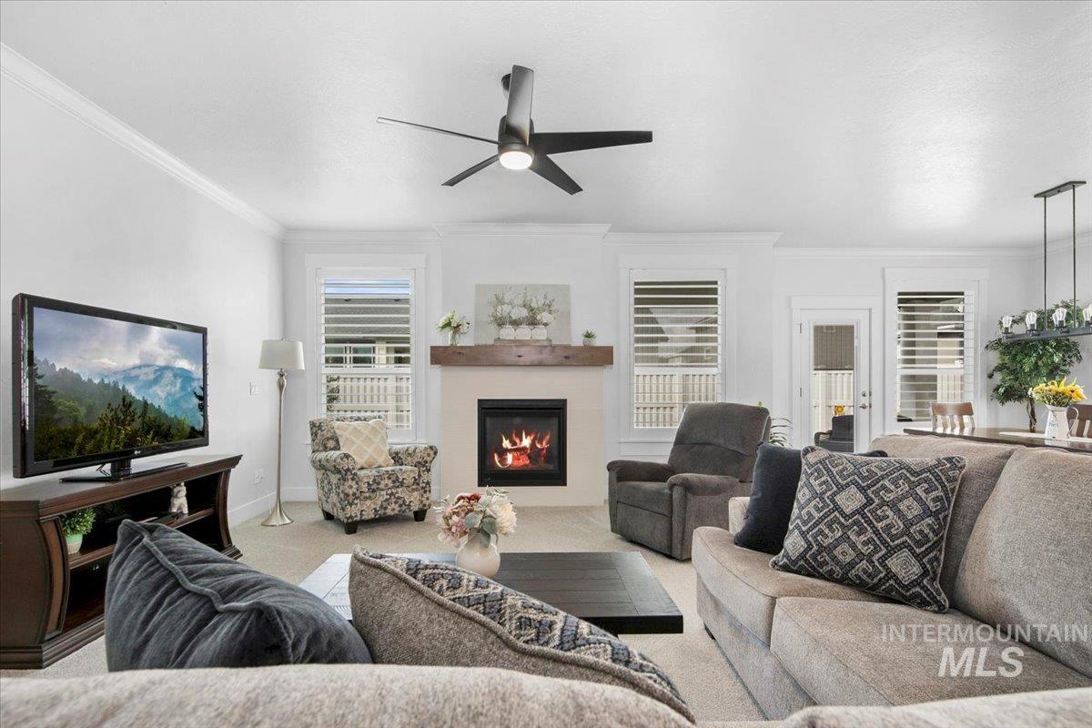 Carpeted living room with a glass covered fireplace, crown molding, and a ceiling fan