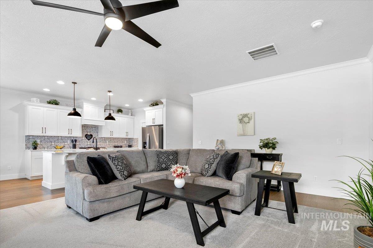 Living room featuring crown molding, light wood-type flooring, a textured ceiling, ceiling fan, and recessed lighting