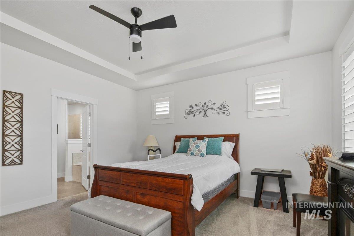 Bedroom featuring a tray ceiling, light carpet, ensuite bathroom, and a ceiling fan