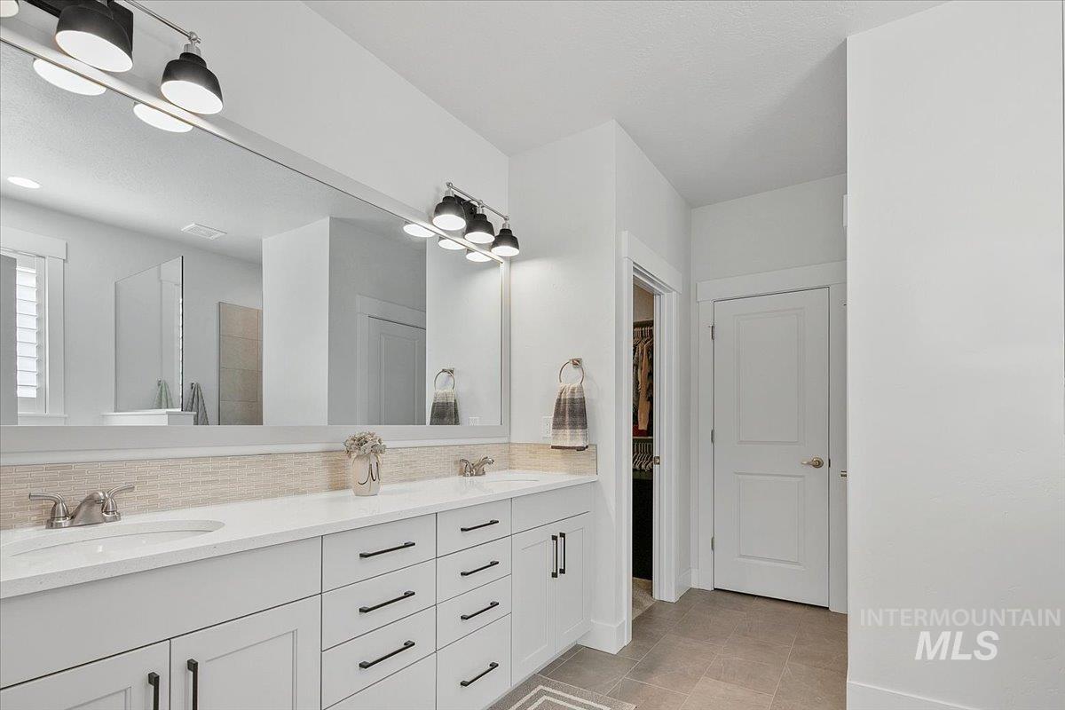 Full bath featuring double vanity, a walk in shower, backsplash, a spacious closet, and light tile patterned floors