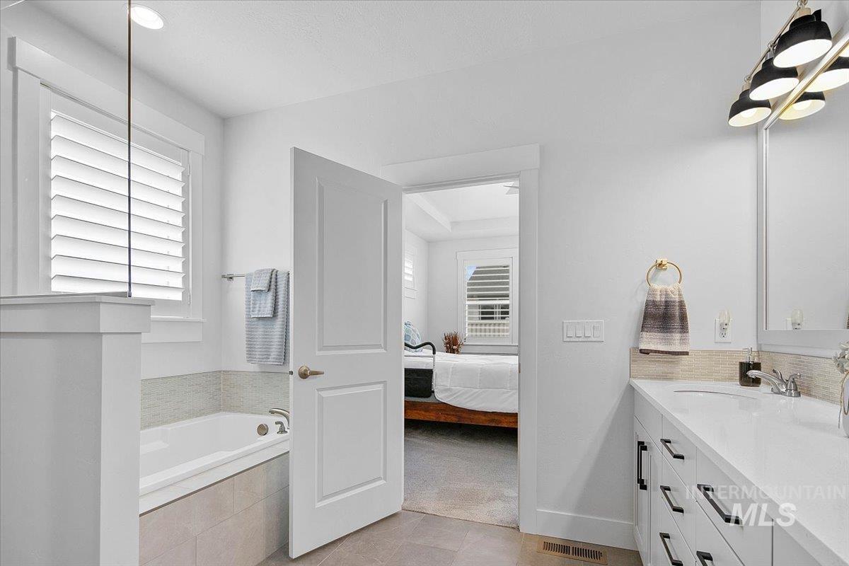Ensuite bathroom with vanity, a garden tub, healthy amount of natural light, and light tile patterned flooring