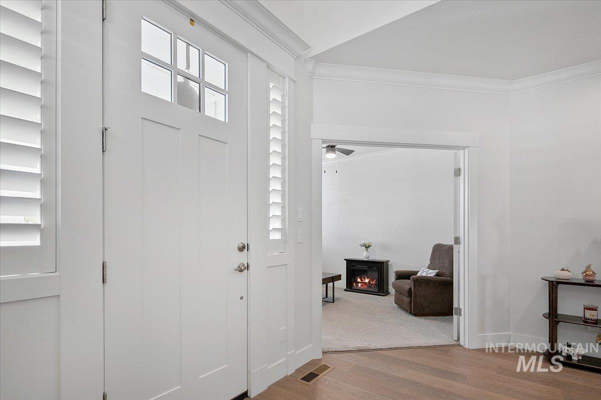 Foyer featuring crown molding, wood finished floors, and a warm lit fireplace