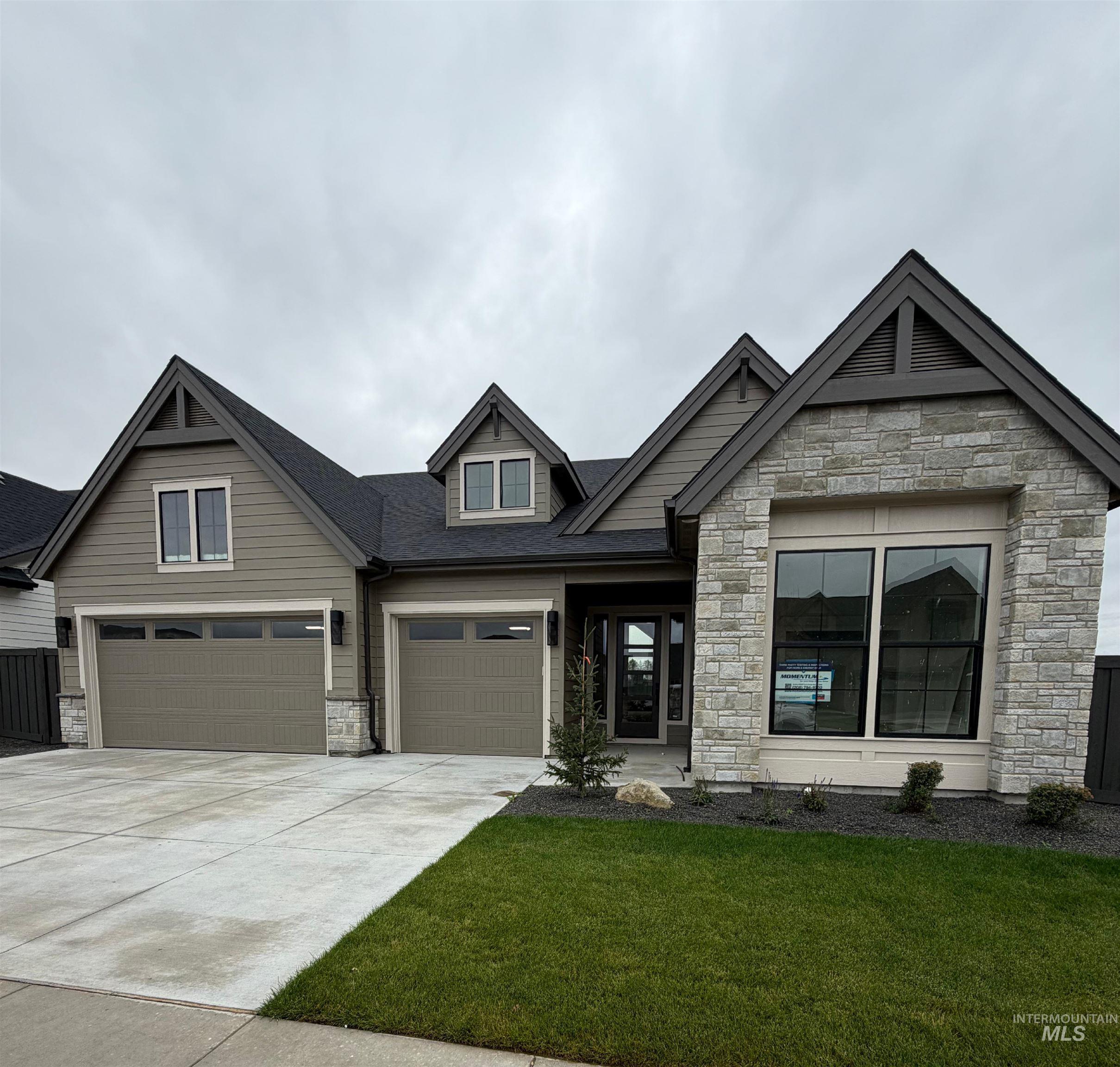 View of front facade with stone siding, concrete driveway, a front yard, an attached garage, and roof with shingles