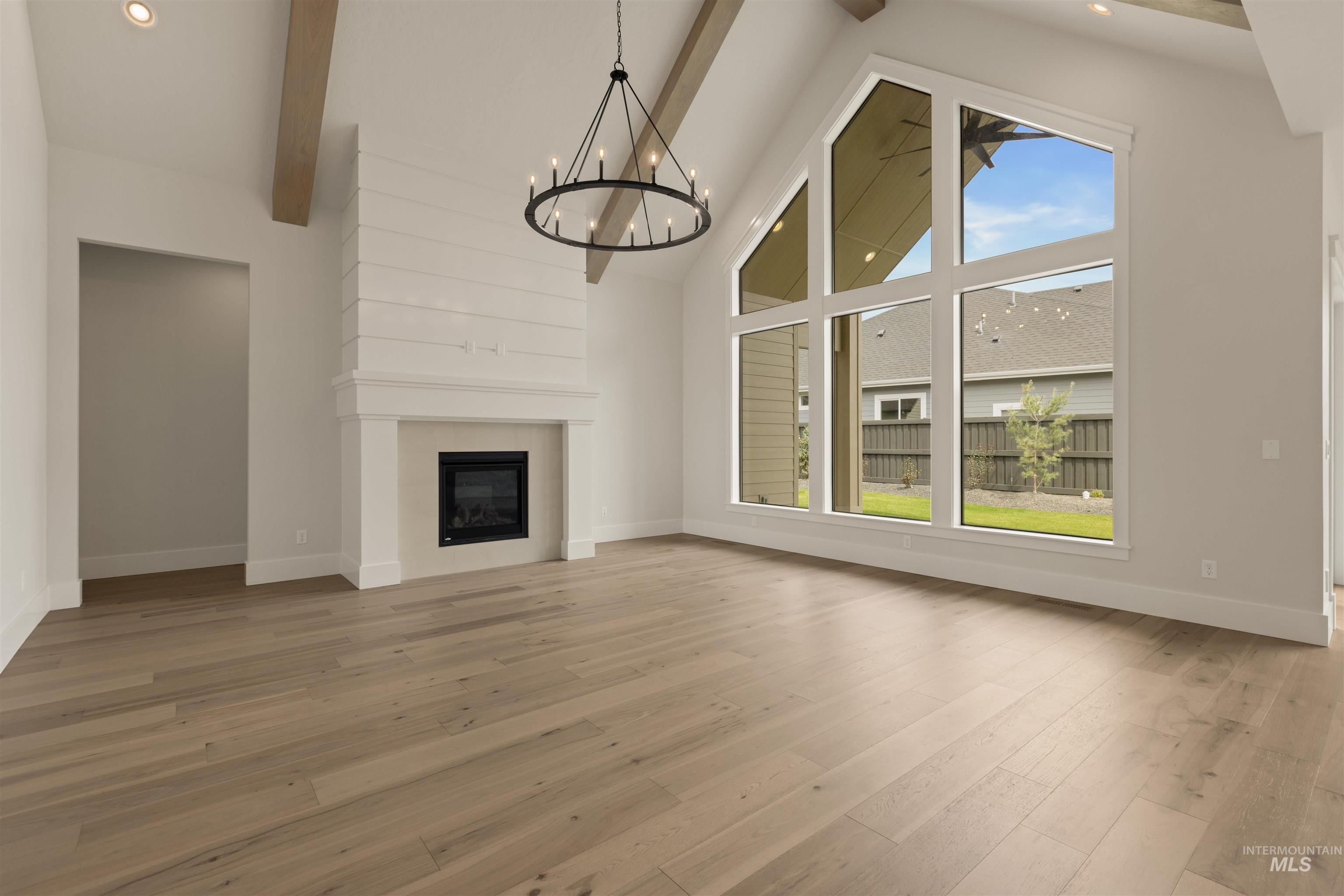 Unfurnished living room featuring high vaulted ceiling, beamed ceiling, a fireplace, light wood-type flooring, and a chandelier
