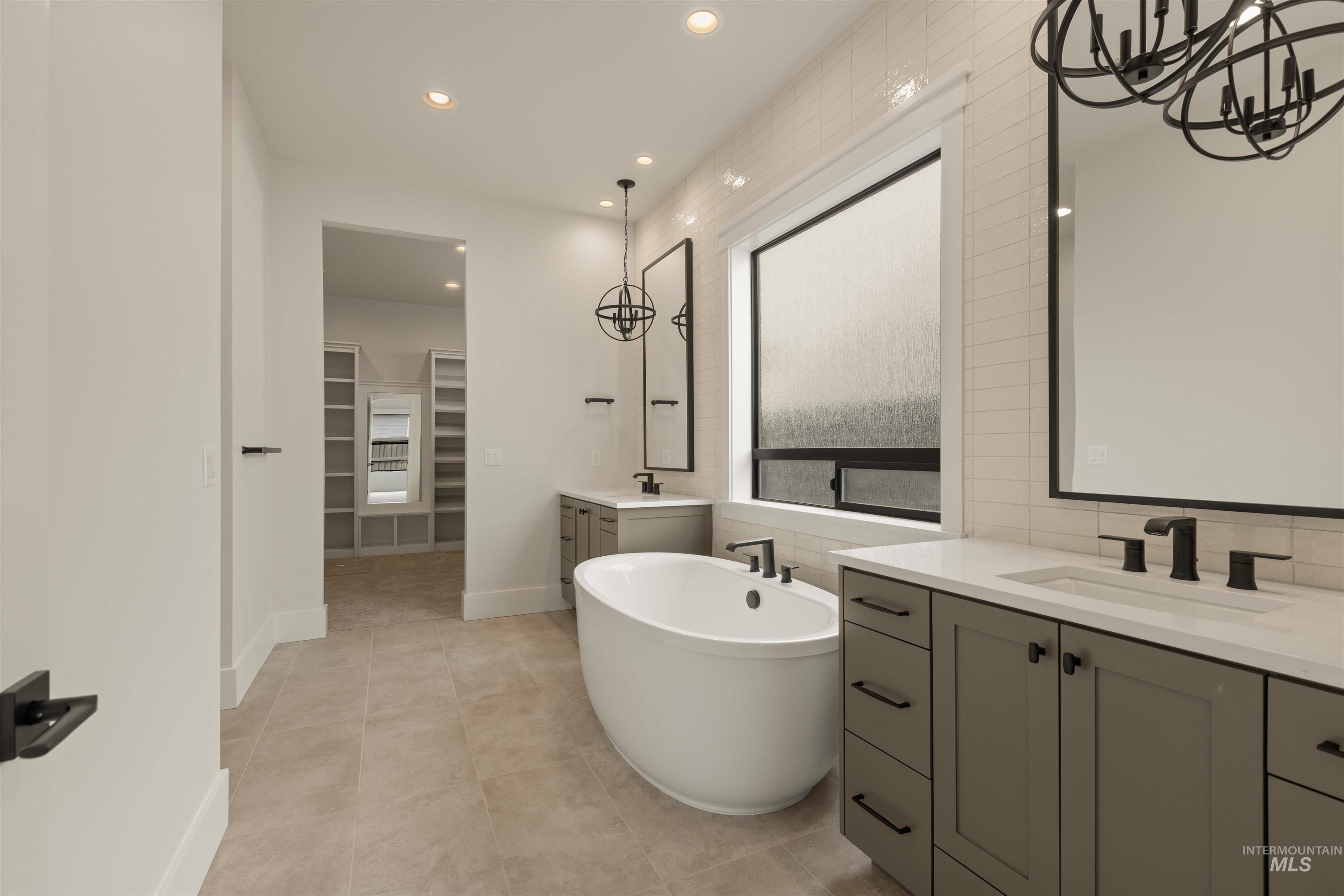 Full bath with a chandelier, two vanities, recessed lighting, a freestanding bath, and a spacious closet