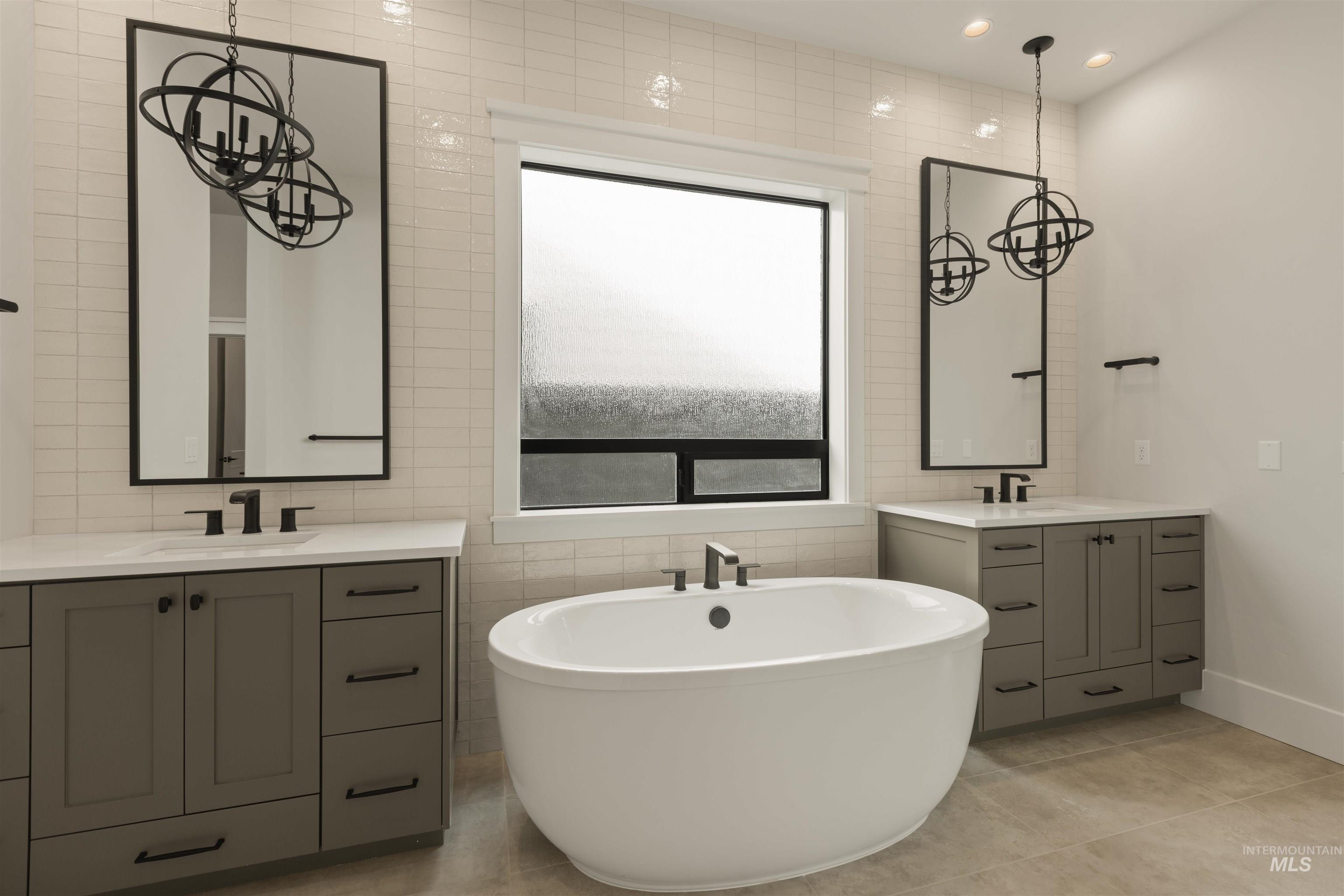 Full bathroom with tile walls, a soaking tub, two vanities, recessed lighting, and light tile patterned floors