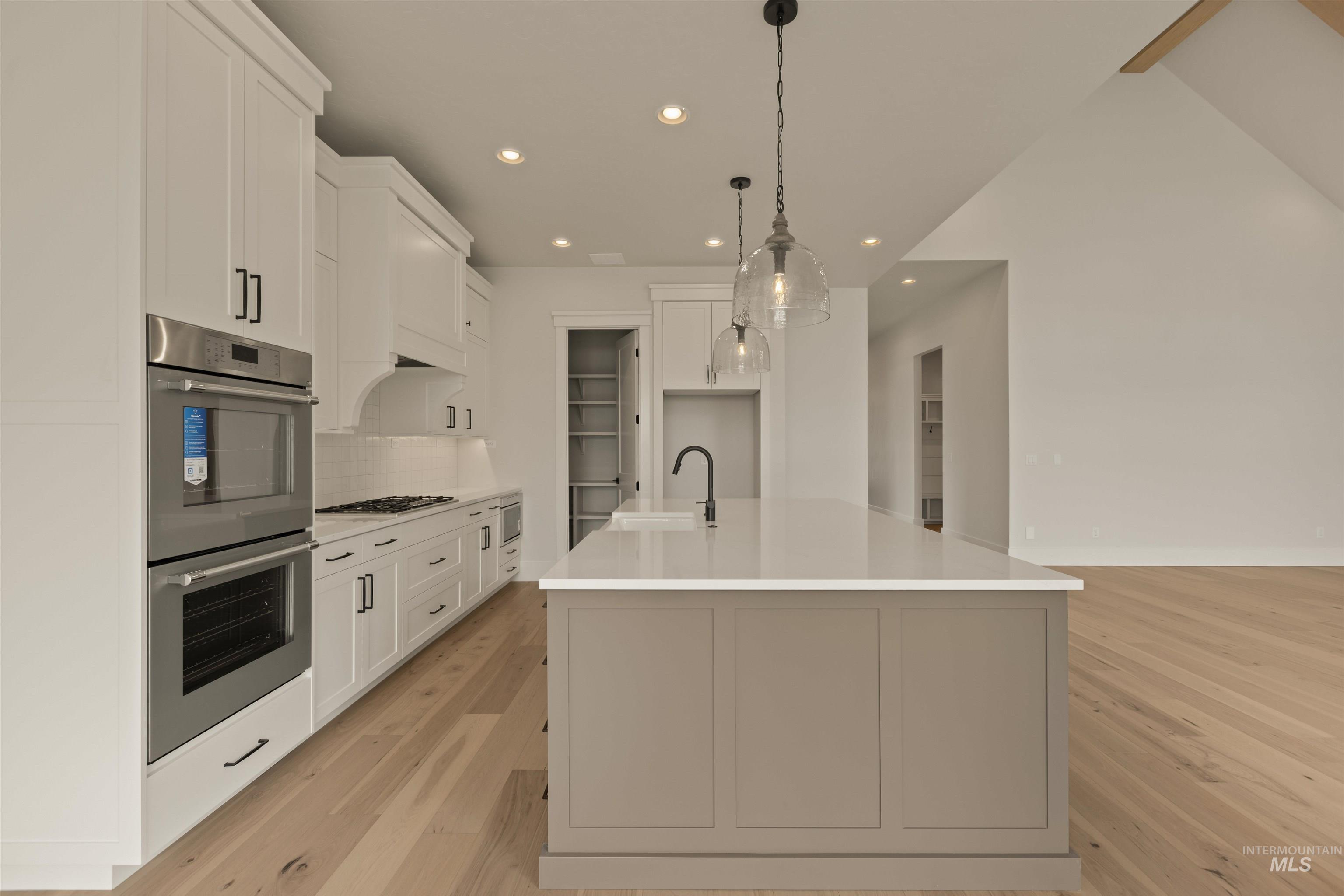 Kitchen featuring recessed lighting, an island with sink, white cabinets, stainless steel double oven, and light wood-style flooring