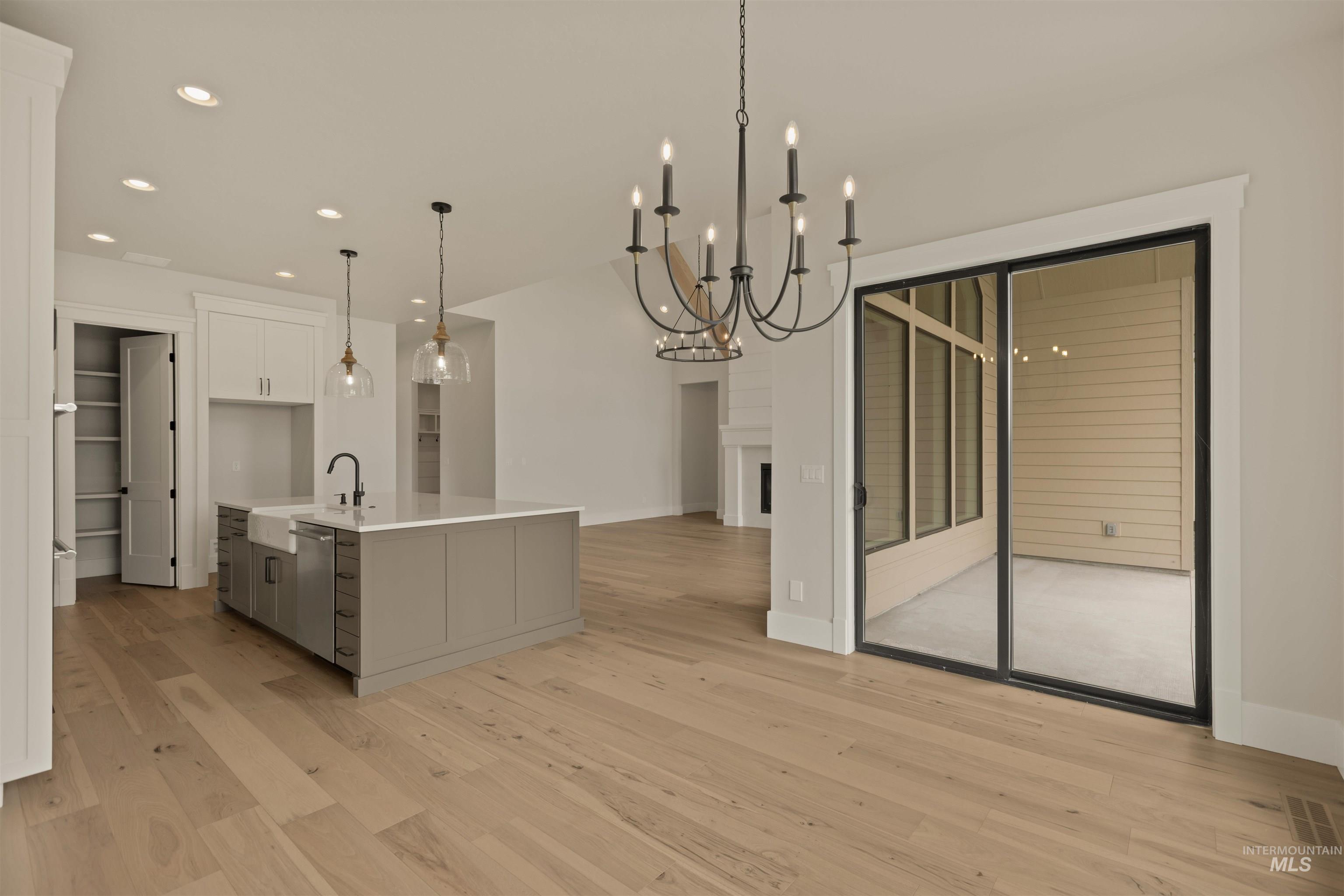 Kitchen with gray cabinetry, recessed lighting, pendant lighting, light wood finished floors, and a center island with sink