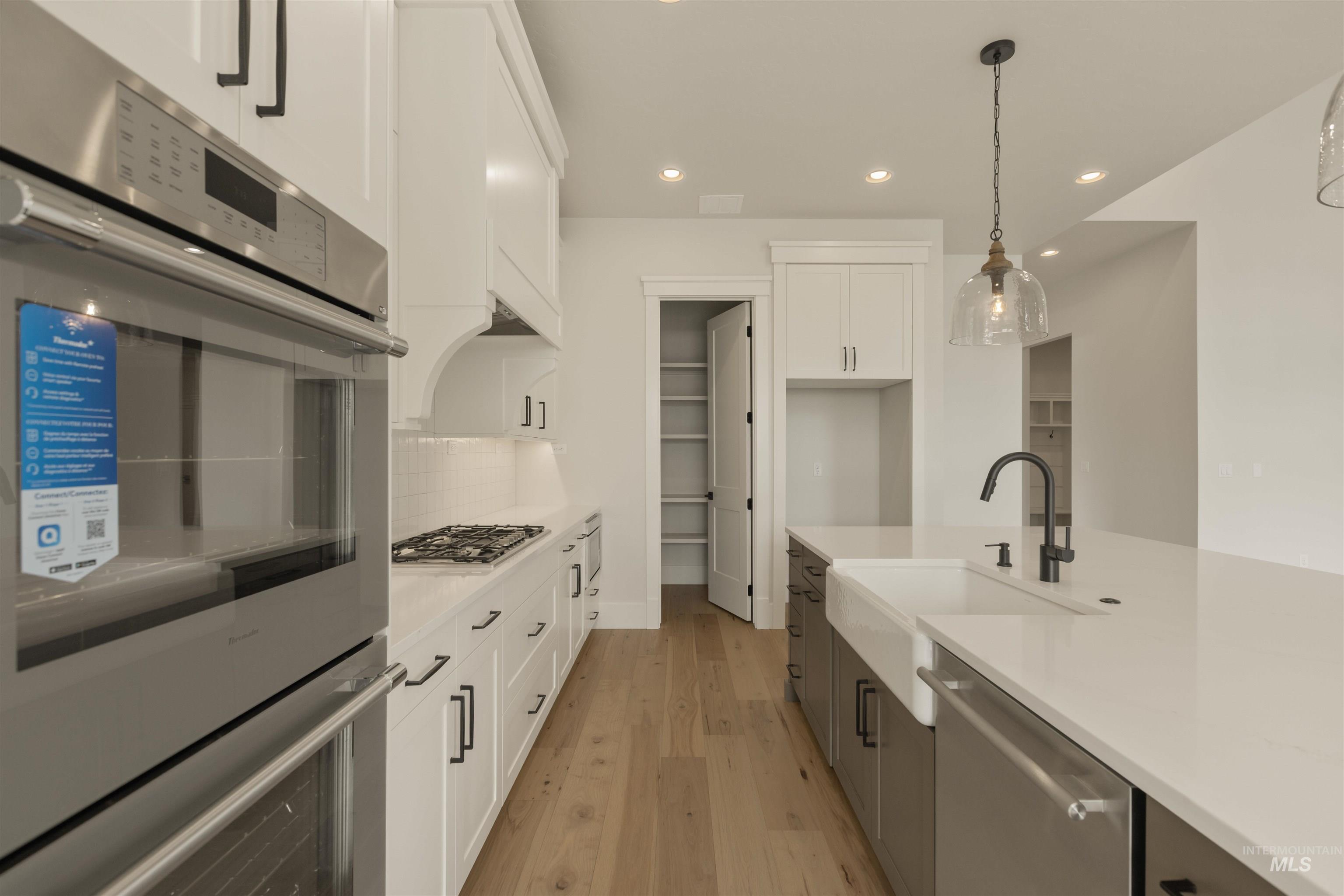 Kitchen with white cabinetry, appliances with stainless steel finishes, recessed lighting, hanging light fixtures, and light wood-type flooring