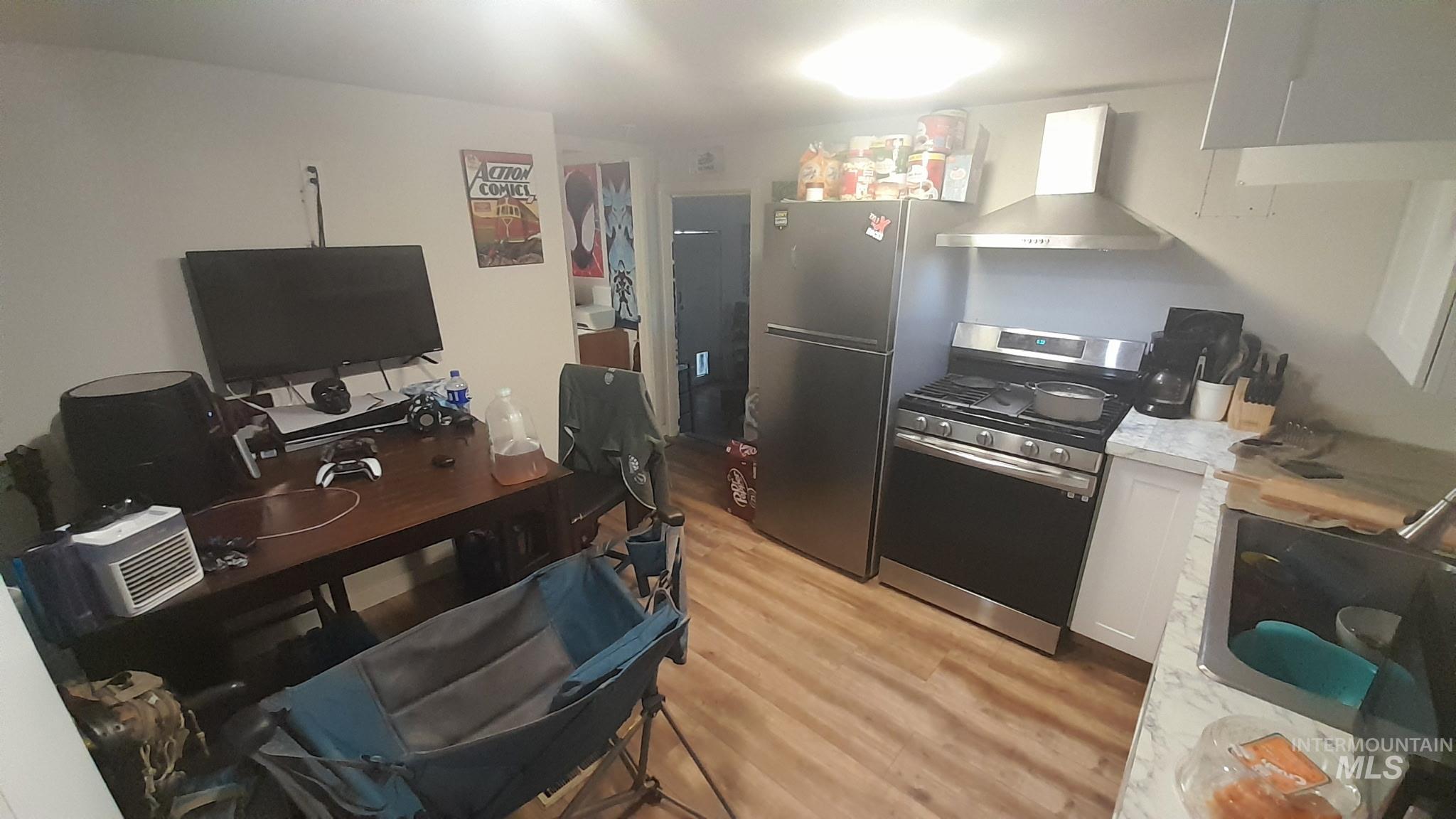 Kitchen featuring stainless steel range with gas stovetop, light countertops, white cabinetry, wall chimney exhaust hood, and a desk