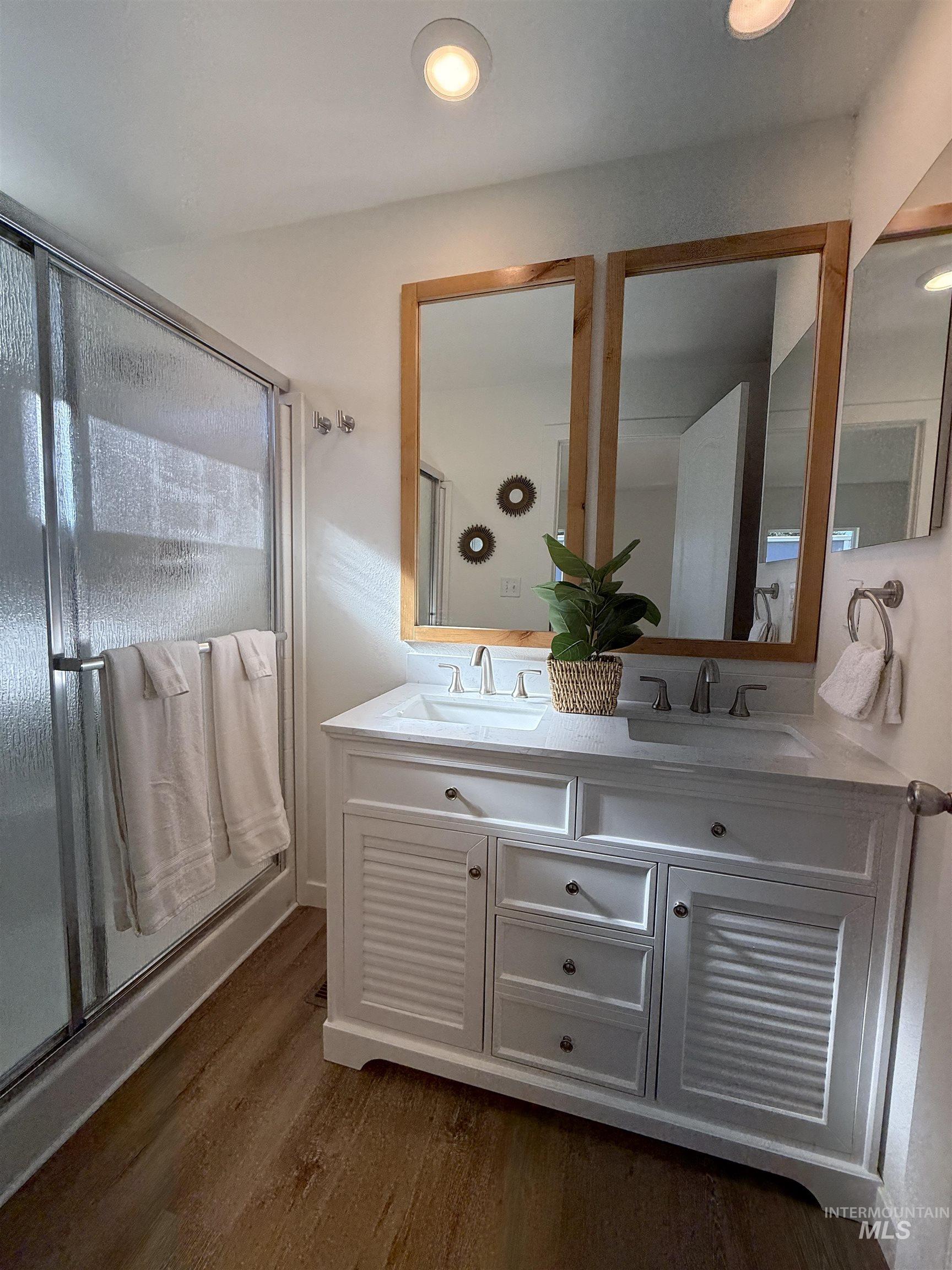 Bathroom featuring dark wood-style floors, double vanity, a shower stall, and recessed lighting