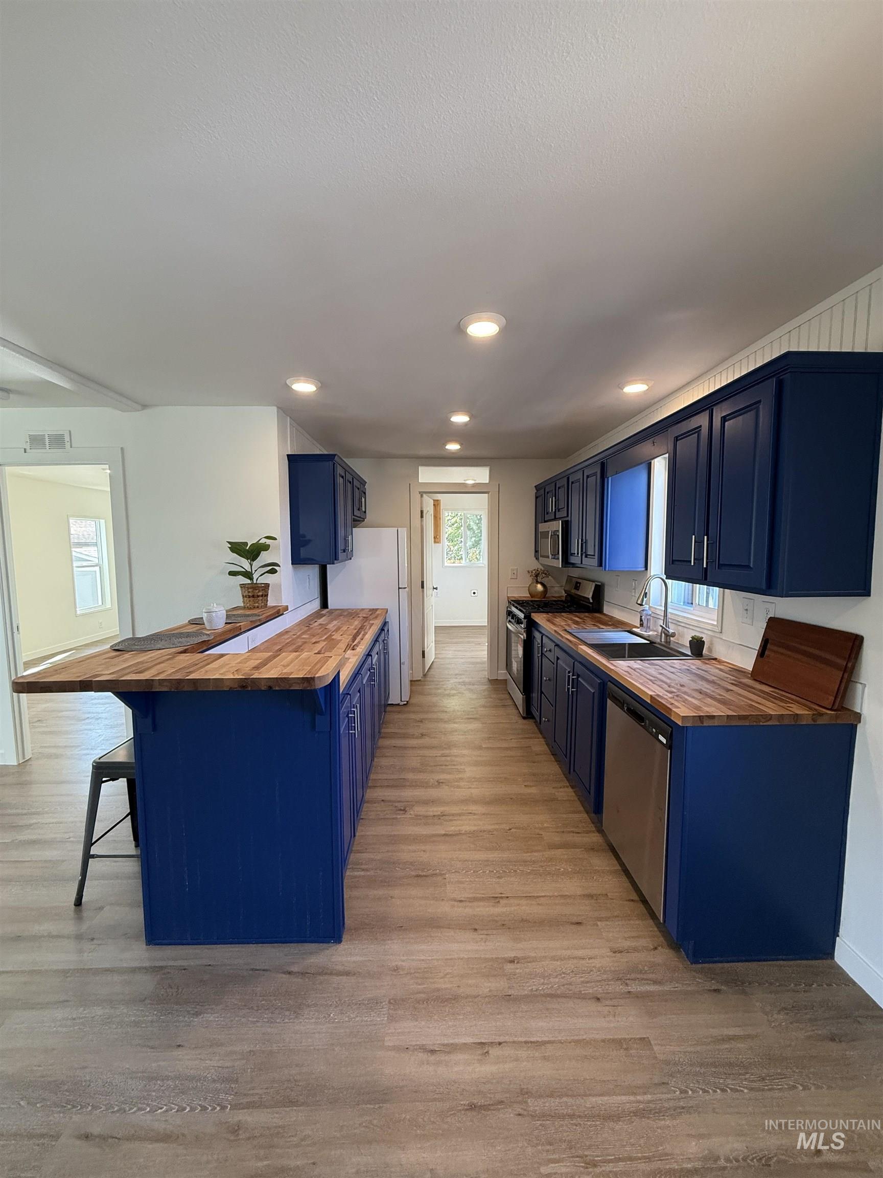 Kitchen with wooden counters, blue cabinets, a kitchen breakfast bar, light wood-type flooring, and recessed lighting