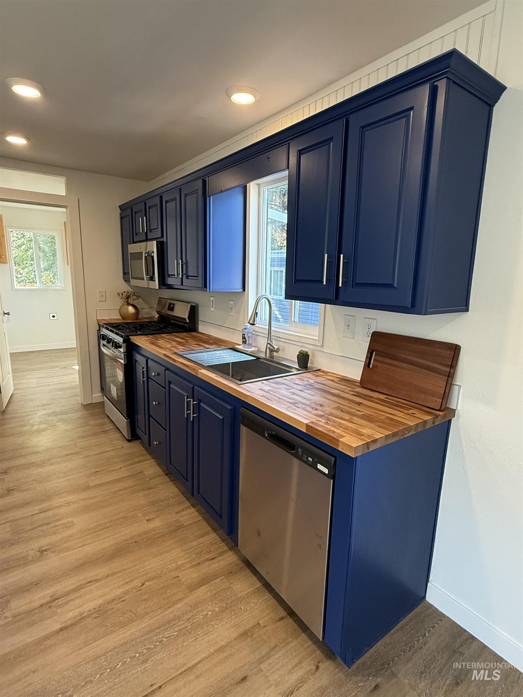 Kitchen featuring butcher block counters, blue cabinetry, appliances with stainless steel finishes, light wood-style floors, and plenty of natural light
