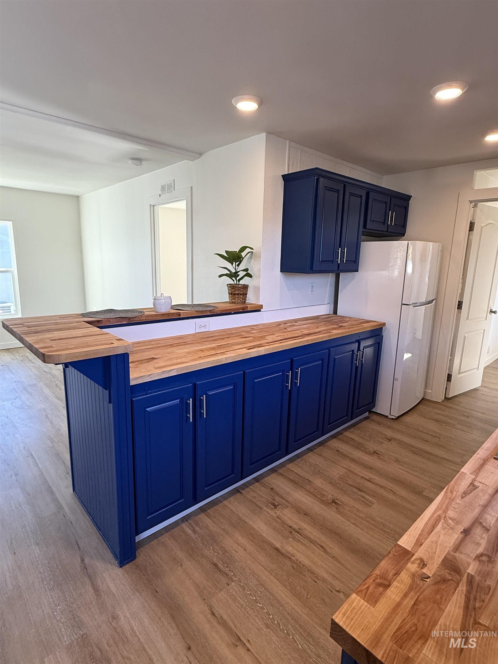 Kitchen with wood counters, freestanding refrigerator, blue cabinetry, dark wood-type flooring, and recessed lighting